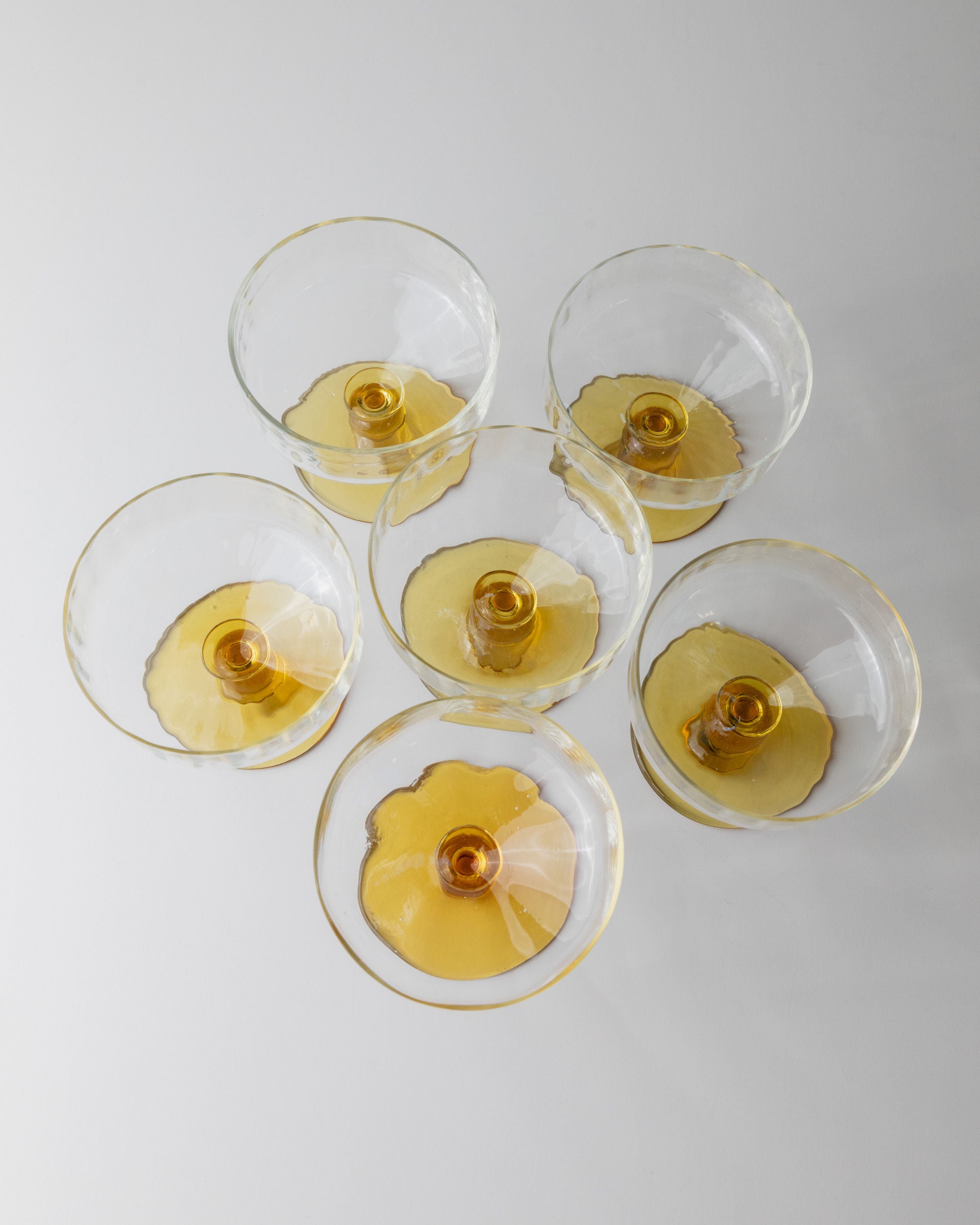 The Set of 6 Murano Glass by Bottega Jacobs, inspired by 70s Italian design, is arranged symmetrically in a hexagonal pattern on a white surface. The glasses' soft shadows enhance the harmonious and visually appealing arrangement.