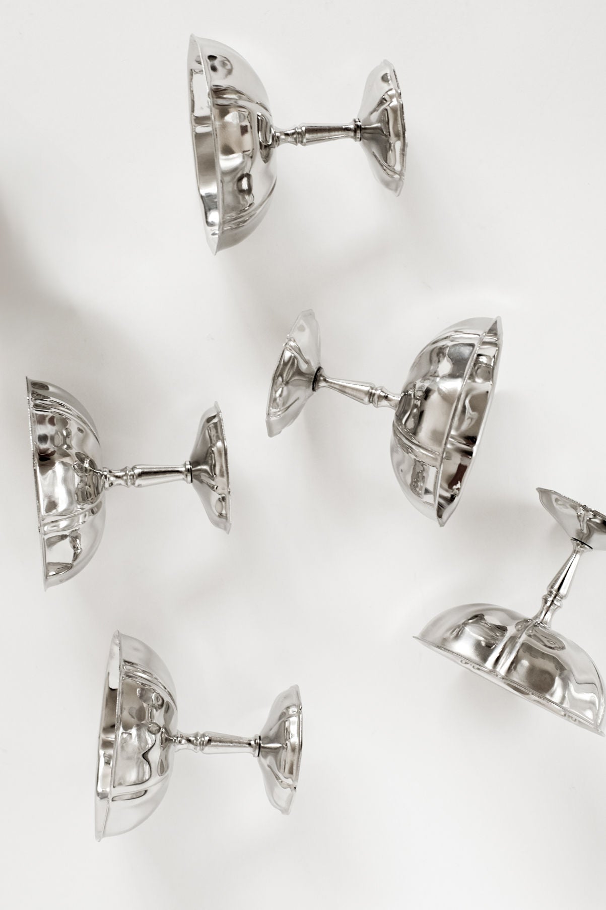 A set of five stainless steel ice coupes from septembre studios, featuring vintage charm, sit upside down on a white surface—their rounded bowls and short stems perfect for serving ice cream.