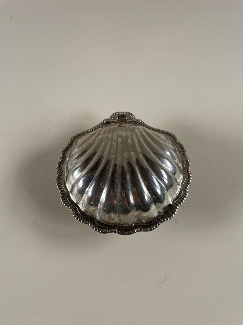 On a simple, light background, the Maud Vaughan Vintage Silver Shell Plate Caviar/Butter Dish displays its ridged design and decorative edging. The metallic surface reflects light, elegantly enhancing its intricate details to complement any table setting.