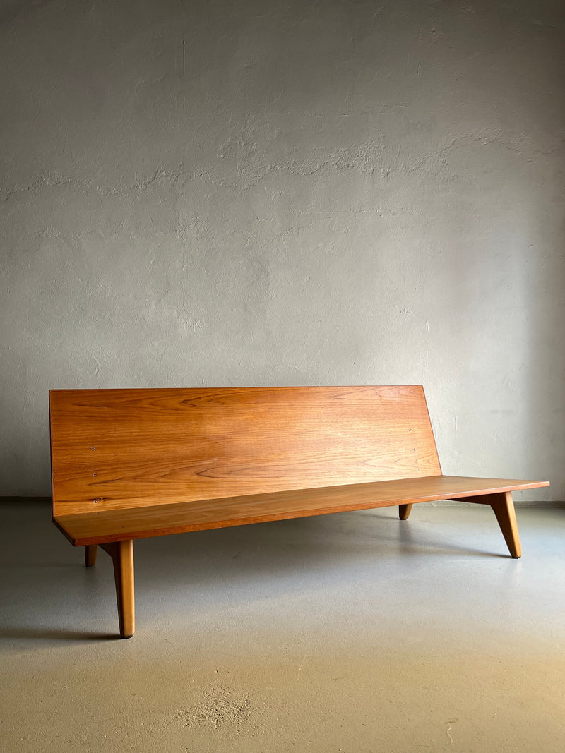 A sleek, minimalist Teak Daybed Sofa by Gustaf Hiort Af Ornäs | Finland | 1950s from Veter Vintage with teak boards and angled legs is placed against a plain wall in a softly lit room. The piece features a smooth, polished surface and simple, modern design lines that evoke vintage condition while maintaining contemporary elegance.