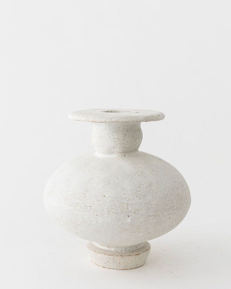 The Calpide Blanco Hueso by Canoa Lab is a round, off-white ceramic vase with a wide body, narrow neck, and flared rim. Its textured, rustic surface recalls Mediterranean design and the timeless appeal of ancient artifacts.