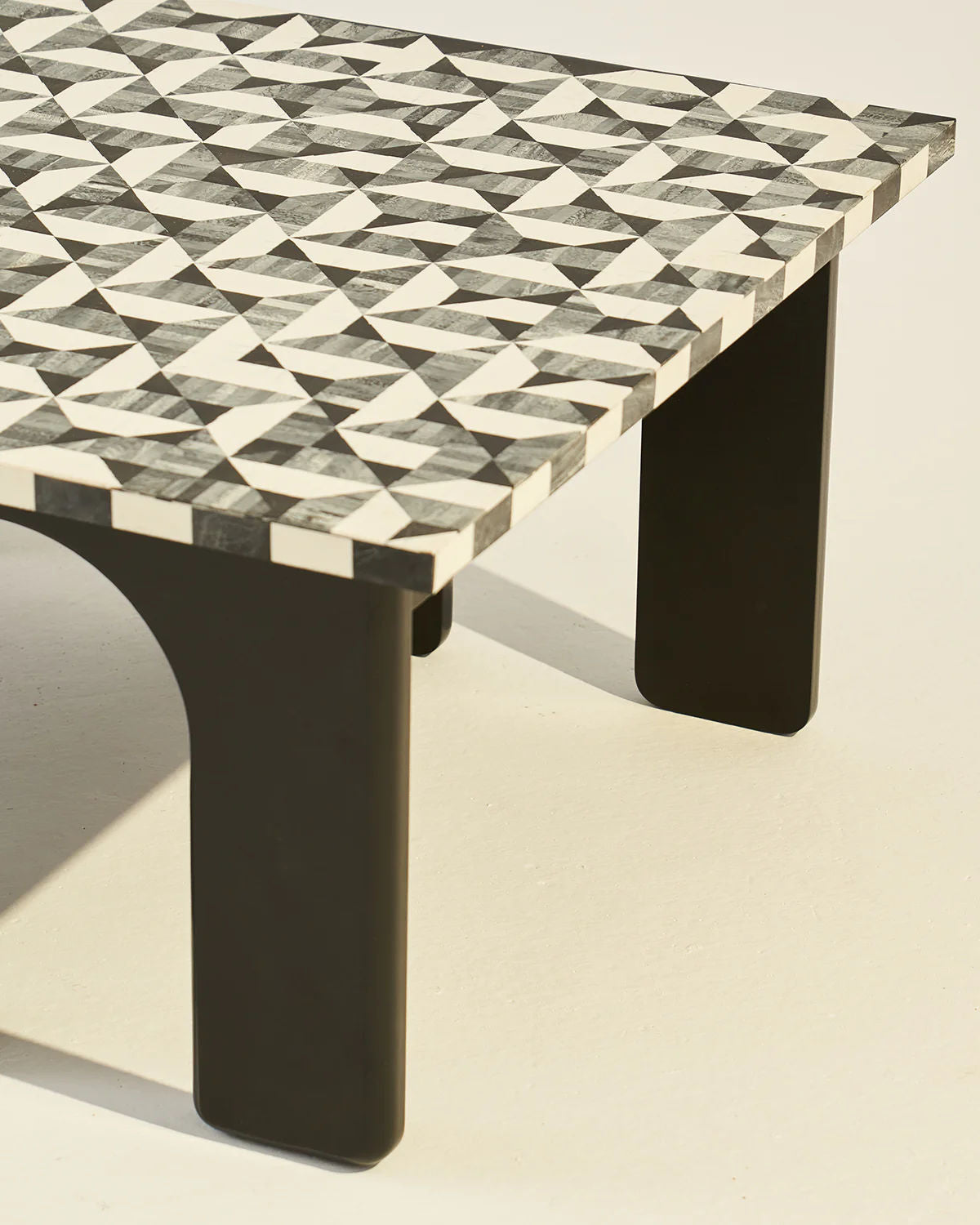 The LMNOH Leo Coffee Table features a striking geometric design with black and white triangular patterns reminiscent of bone inlay craftsmanship. It stands on robust black legs, casting a subtle shadow on the light-colored floor.