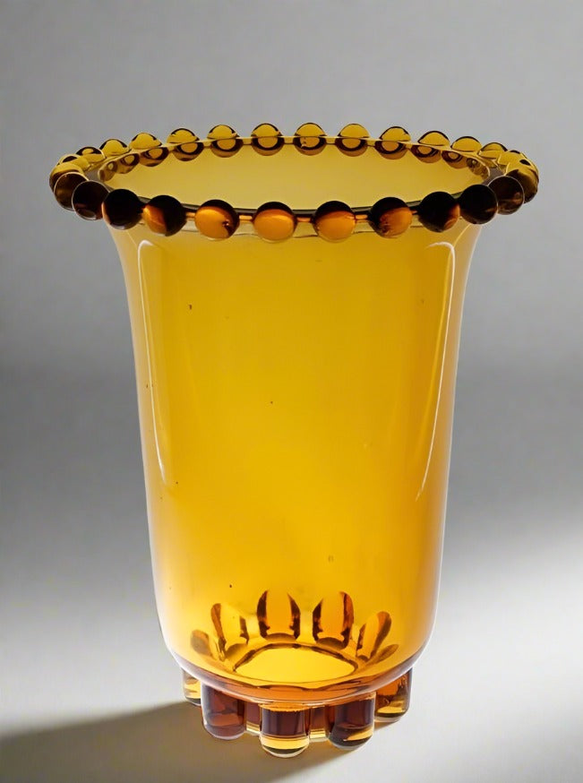 The Art Deco Amber Glass Vase by Rudolf Schrotter from Flock Studio, crafted from translucent amber glass, boasts a flared rim and decorative rounded protrusions along the edge, reminiscent of vintage Art Deco design. The light filters through the glass, casting a warm glow against a neutral background.