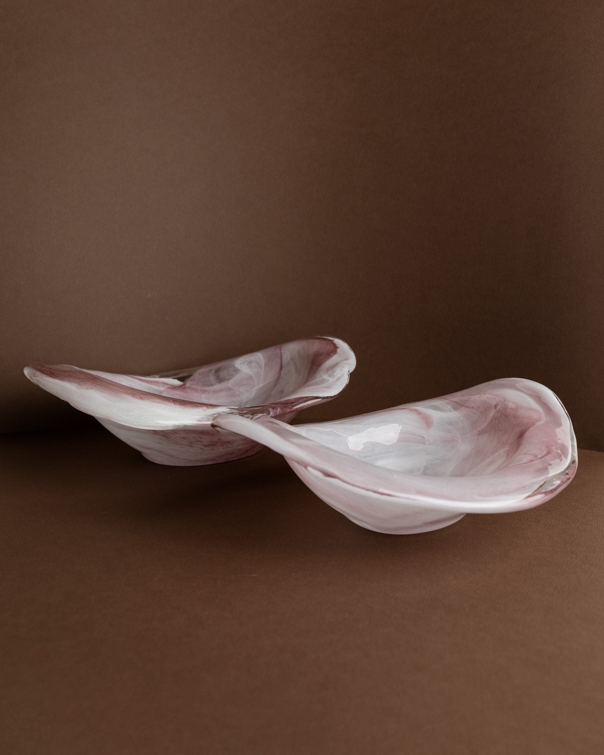 The Murano Glass Bowls by Bottega Jacobs, Italy 1970s, feature a marbled pink and white glaze with wavy edges, echoing vintage Italian design against a brown surface and matching background.