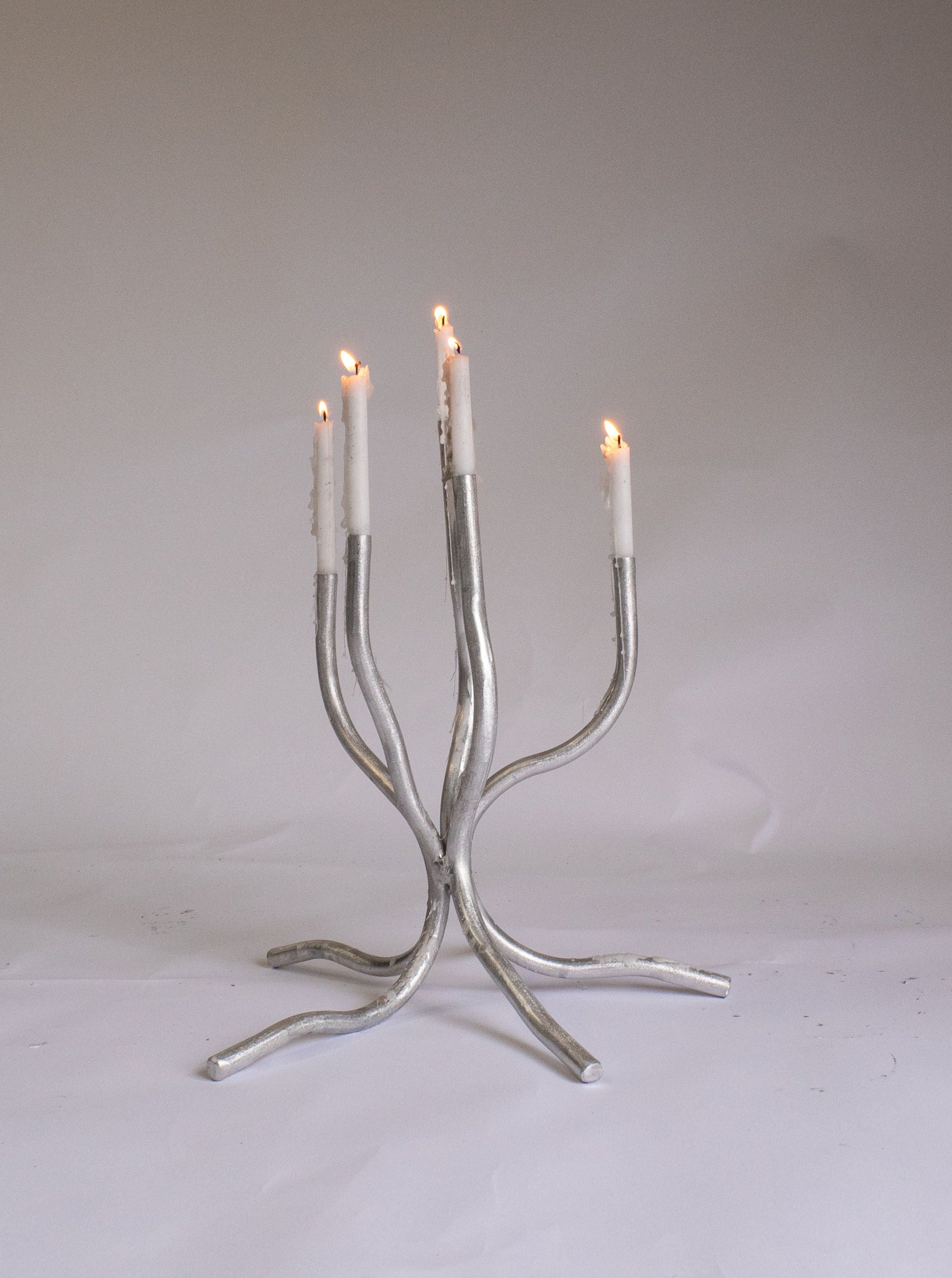 A modern, hand-made Small Candelabra by Six Dots Design with a branched design, displaying four lit taper candles against a plain, light background.