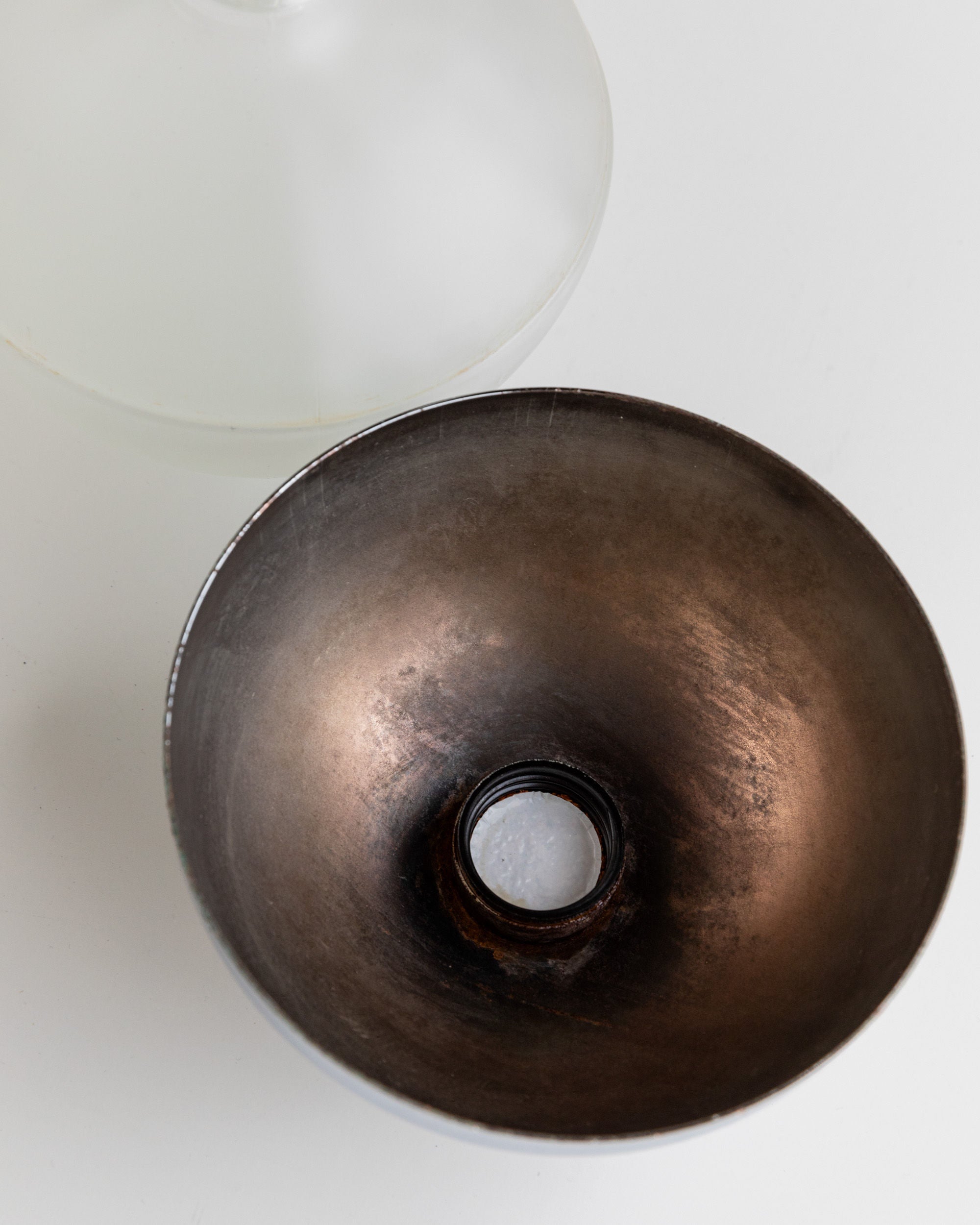 A metallic, bowl-shaped object with a small circular opening at the bottom reflects space age design on the white surface. A frosted glass object, resembling Bottega Jacobs' Liqueur Bottle from Italy 1980s, is partially visible in the background.