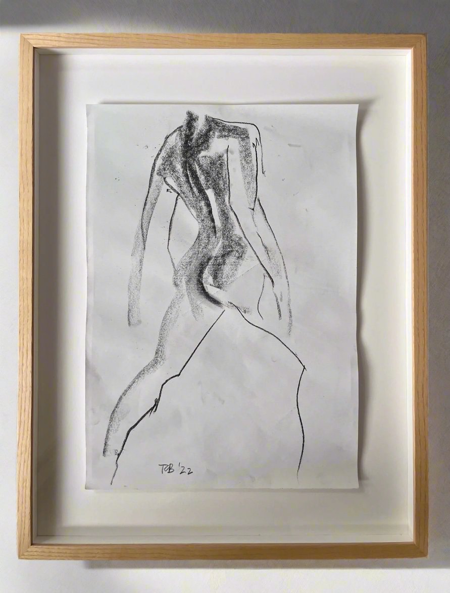 A minimalist black-and-white charcoal artwork titled "Croquis Drawing no.IX" by Médecine, featuring a male nude torso, displayed in a light wooden frame with a white mat. The abstract sketch boasts fluid lines and subtle shading. It is signed "TB '22" at the bottom, emphasizing the contemporary artist’s style.