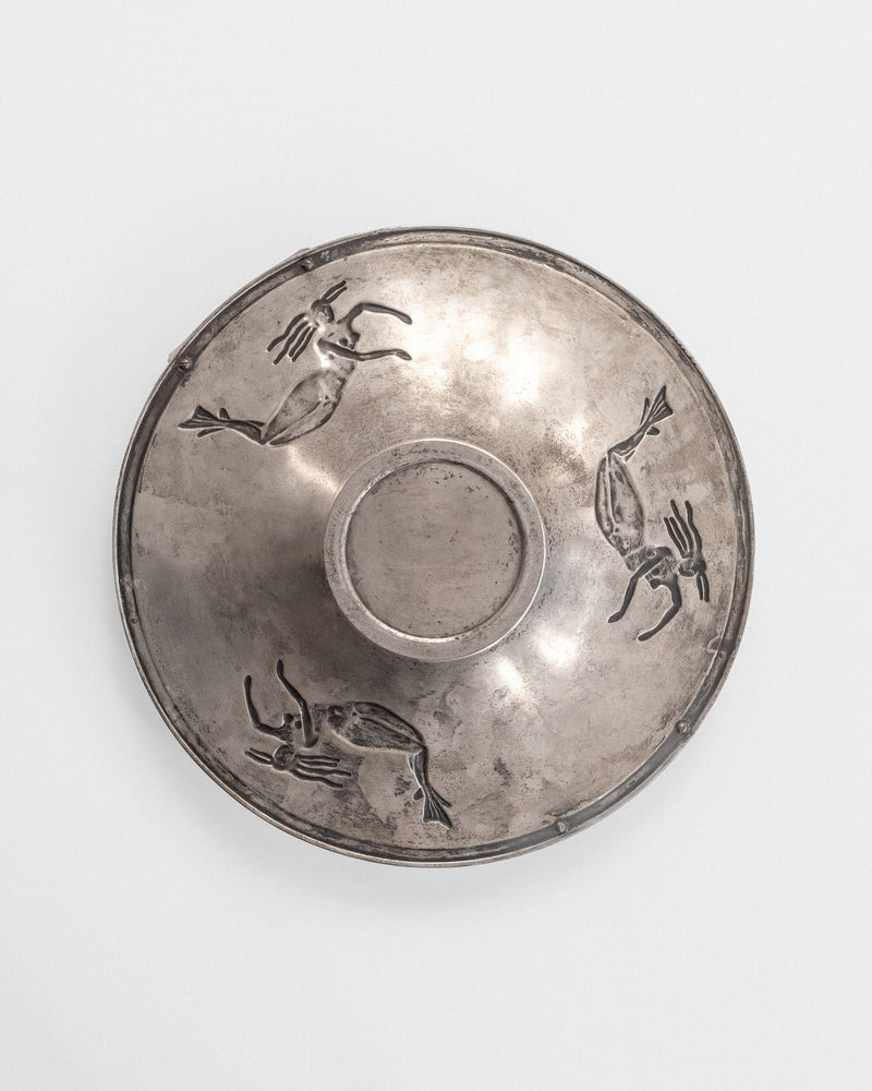 The Decorative Bowl with Mermaids by Spigel, from the 1930s, is a round, silver-plated piece featuring engraved images of four antelopes in a running posture around the edge against a plain background. This elegant and shiny bowl embodies the Swedish Grace style of the Art Deco period.
