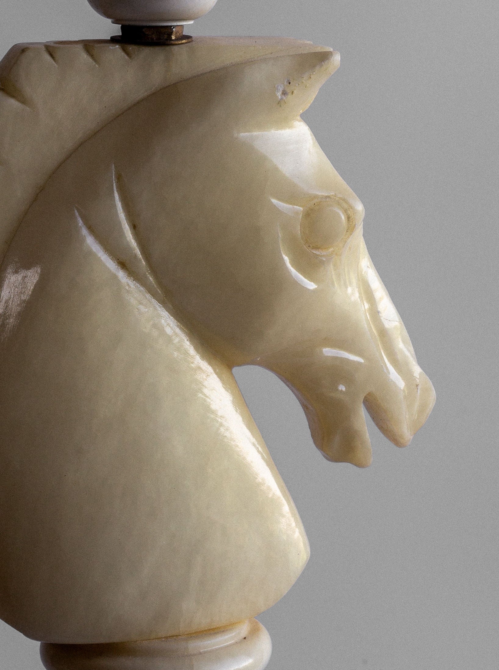 A carved chess knight piece, crafted from polished white alabaster, sits against a plain gray background. The intricate details highlight the horse's mane and facial features, reminiscent of the ornate Spigel White Knight Alabaster Table Lamp from Italy in the 1970s.