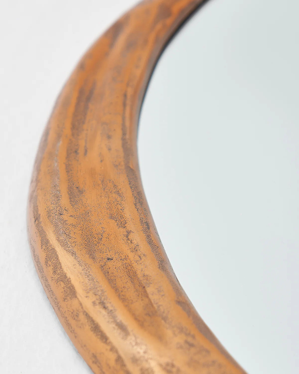 This is a close-up of the Rizzo Mirror by LMNOH, featuring a textured, natural wood-like frame that exudes modern aesthetics with its warm, earthy tone and smooth curved edges. The mirror surface softly reflects light.