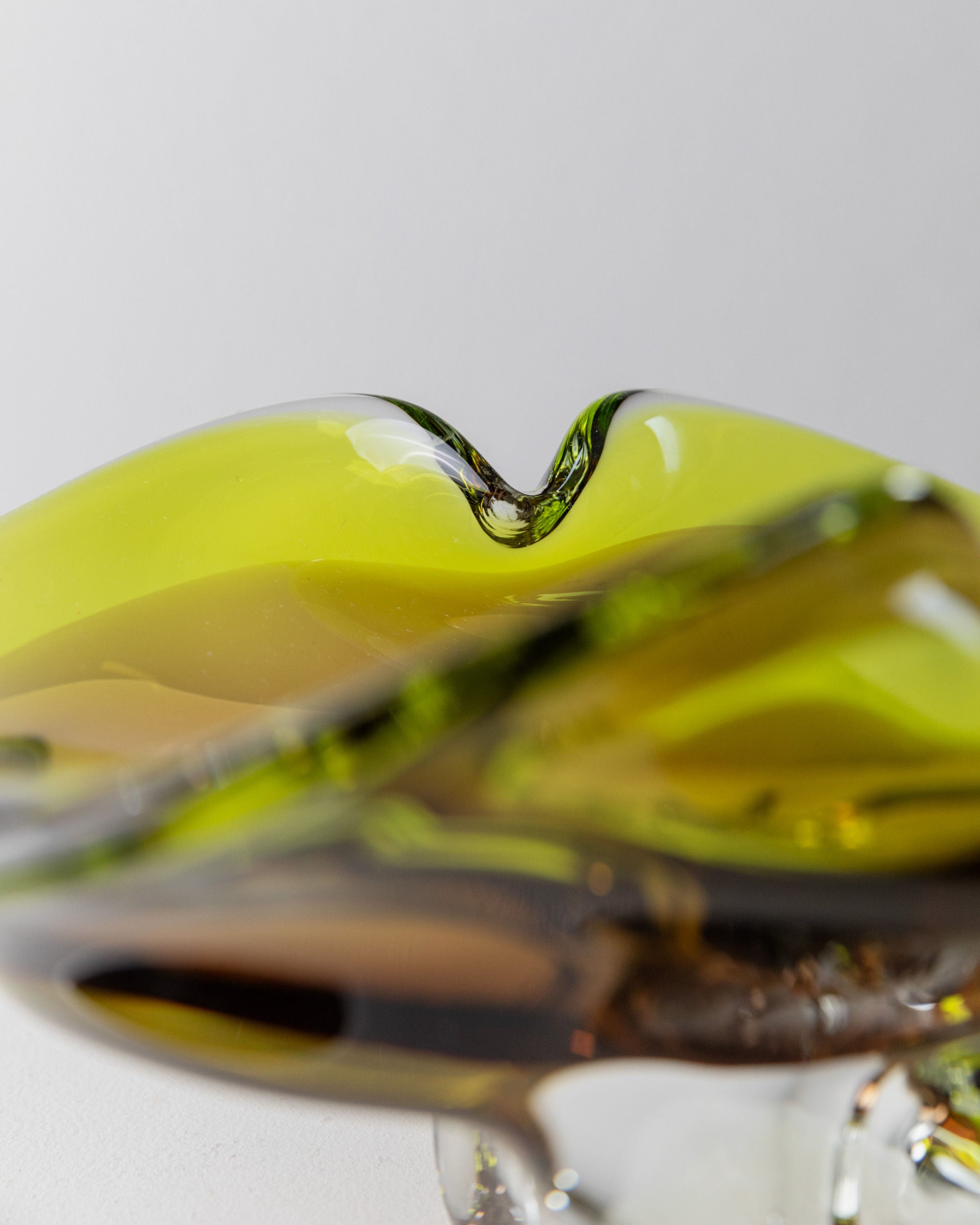A close-up of the Murano Glass Bowl by Bottega Jacobs, Italy 1970s, showcases its vintage-inspired shape in green and brown hues. Smooth curves and a glossy finish reflect light, highlighting the exquisite translucent quality and Italian craftsmanship against a plain background.