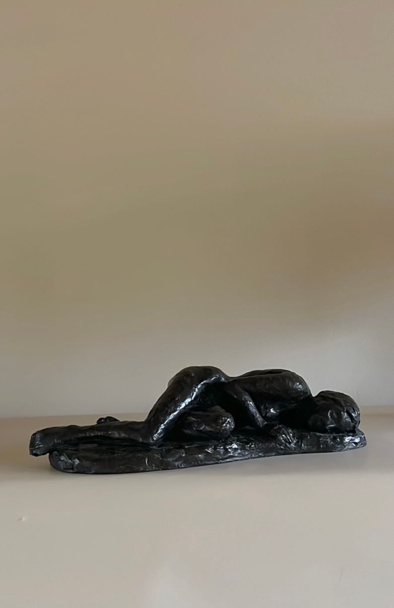 Plaster sculpture by Maud Vaughan featuring a reclining nude figure in a relaxed pose, emphasizing its contours and musculature against a plain background.