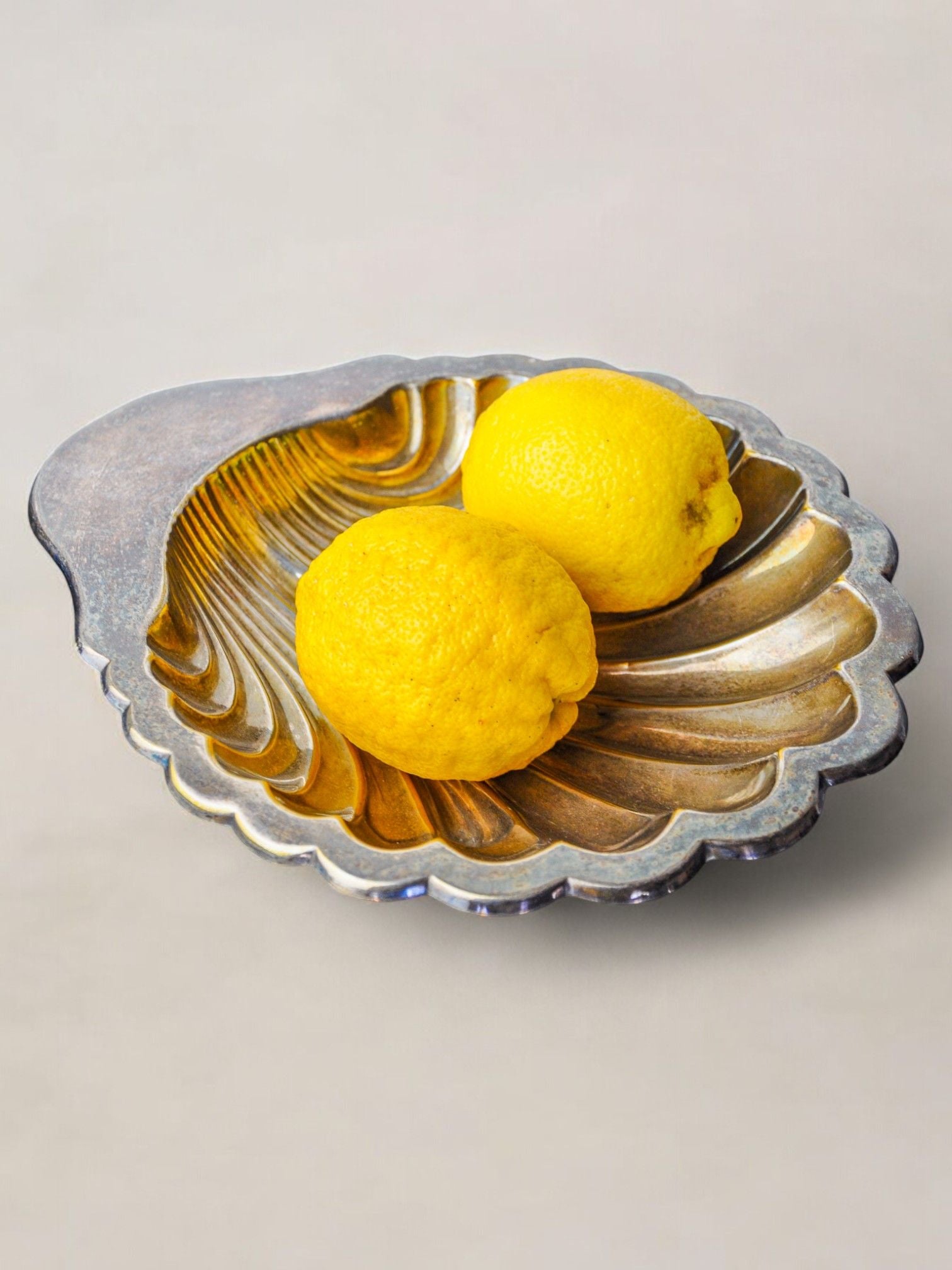 Two bright yellow lemons rest in a stunning Large Shell Shaped Vide-Poche by Malamar Studio, Italy, 1970, on a light gray background, showcasing exquisite design.