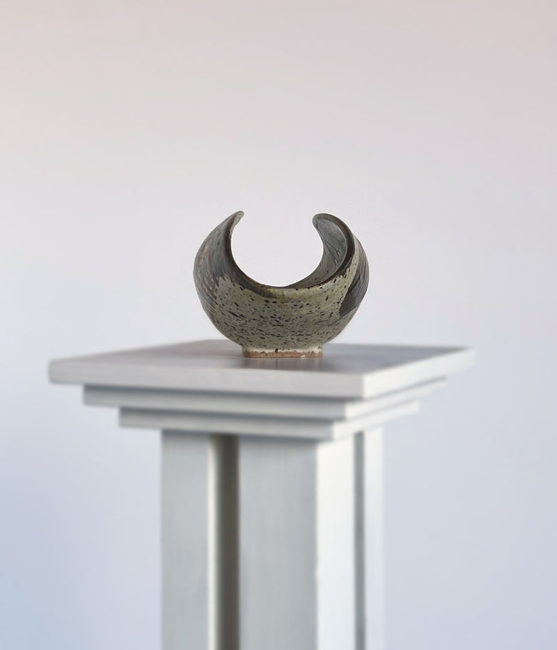 Olive green ceramic sculptural dish with textured surface on white pedestal