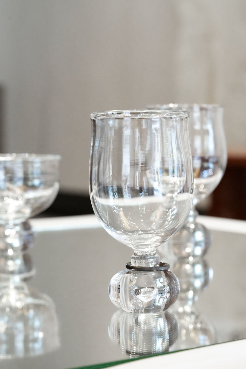 Clear crystal wine glasses with decorative bubble stems on mirrored surface