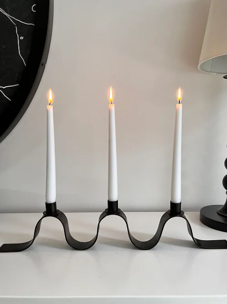 Black metal ribbon candelabra with three lit white tapered candles