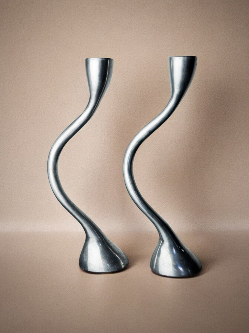 Against a neutral beige background, the Pair of Zigzag Candle Holders 1970 by Malamar Studio stand gracefully with their sleek, modern aluminum design. These rare objects feature twisted curves that create an artistic and captivating look.