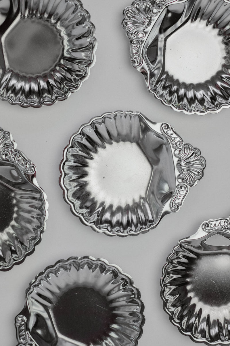 The Set of 6 Small Shell Dishes by septembre studios are displayed on a light gray background. These vintage-condition molds with a shiny finish feature fluted edges and ornate handles, reflecting light and highlighting their unique character.