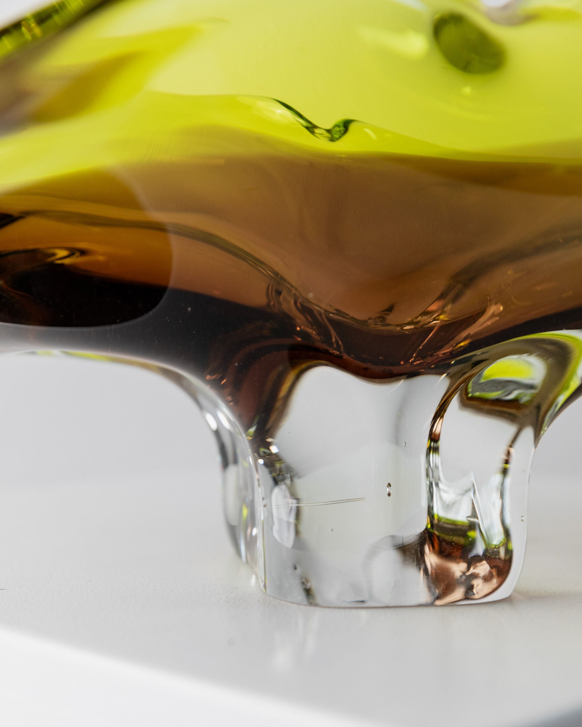 Close-up of a Murano Glass Bowl - Italy 1970s from Bottega Jacobs, showcasing swirling greens, browns, and clear glass. Its smooth and flowing shapes embody Italian craftsmanship in an abstract and elegant design, set against a plain white background.