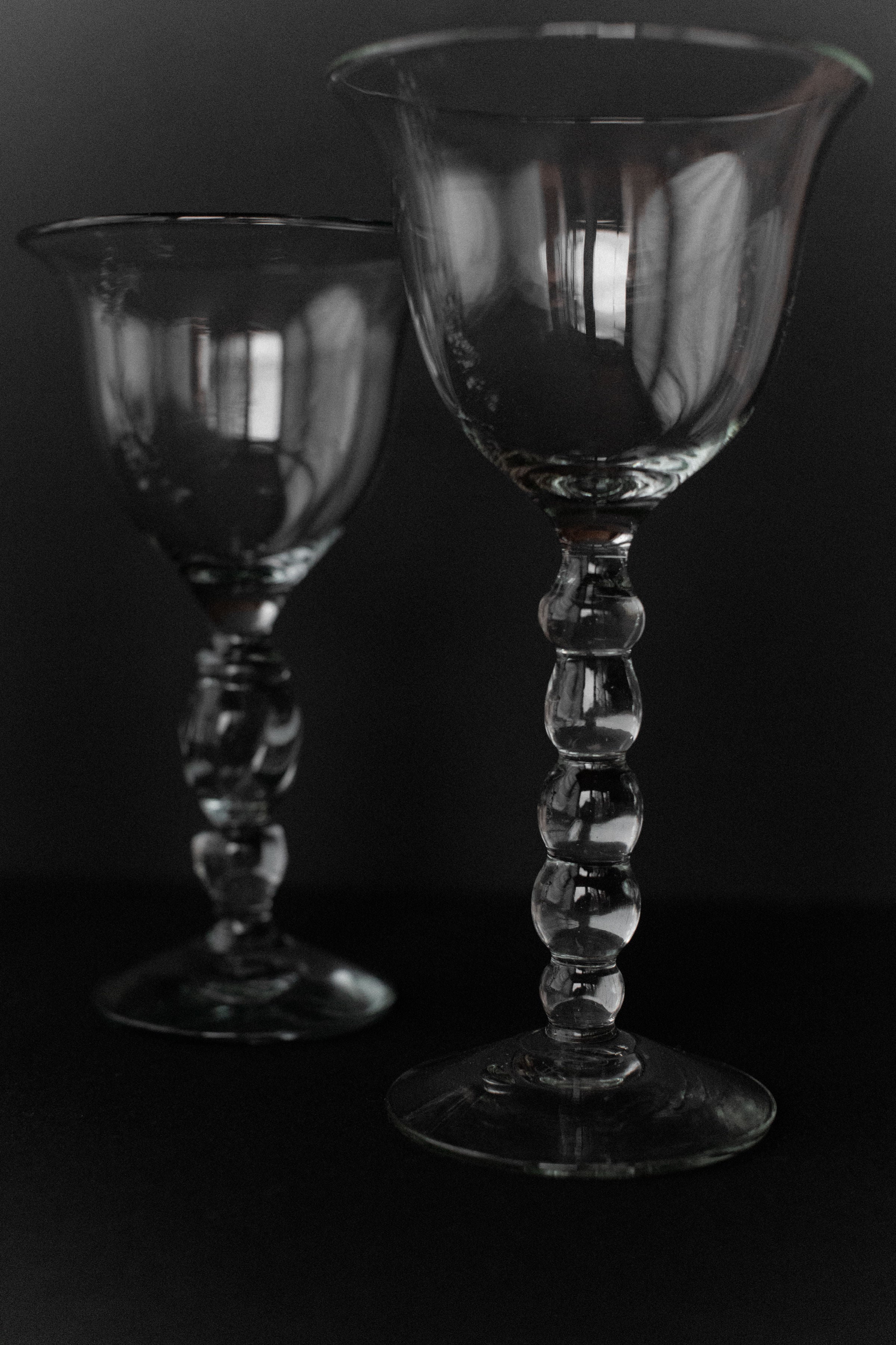 Five handmade art glass goblets from Out For Lunch, with elegantly curved, textured stems and showcasing artisanal craftsmanship, are positioned against a dark background. Light subtly reflects on their surfaces, highlighting their exquisite handmade artistry.