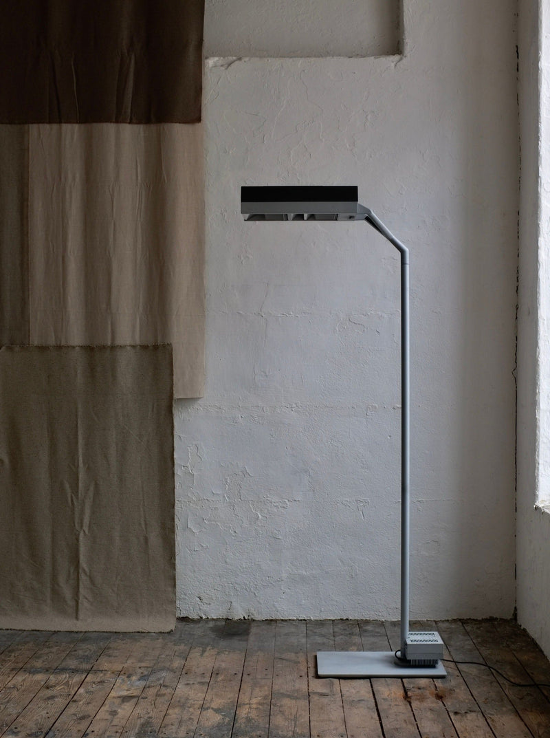 A minimalist Postmodern Metal Lamp by Glen Oliver Löw and Antonio Citterio for Ansorg | 1990s stands in the corner of a room with textured white walls and a worn wooden floor, next to a two-tone hanging fabric.