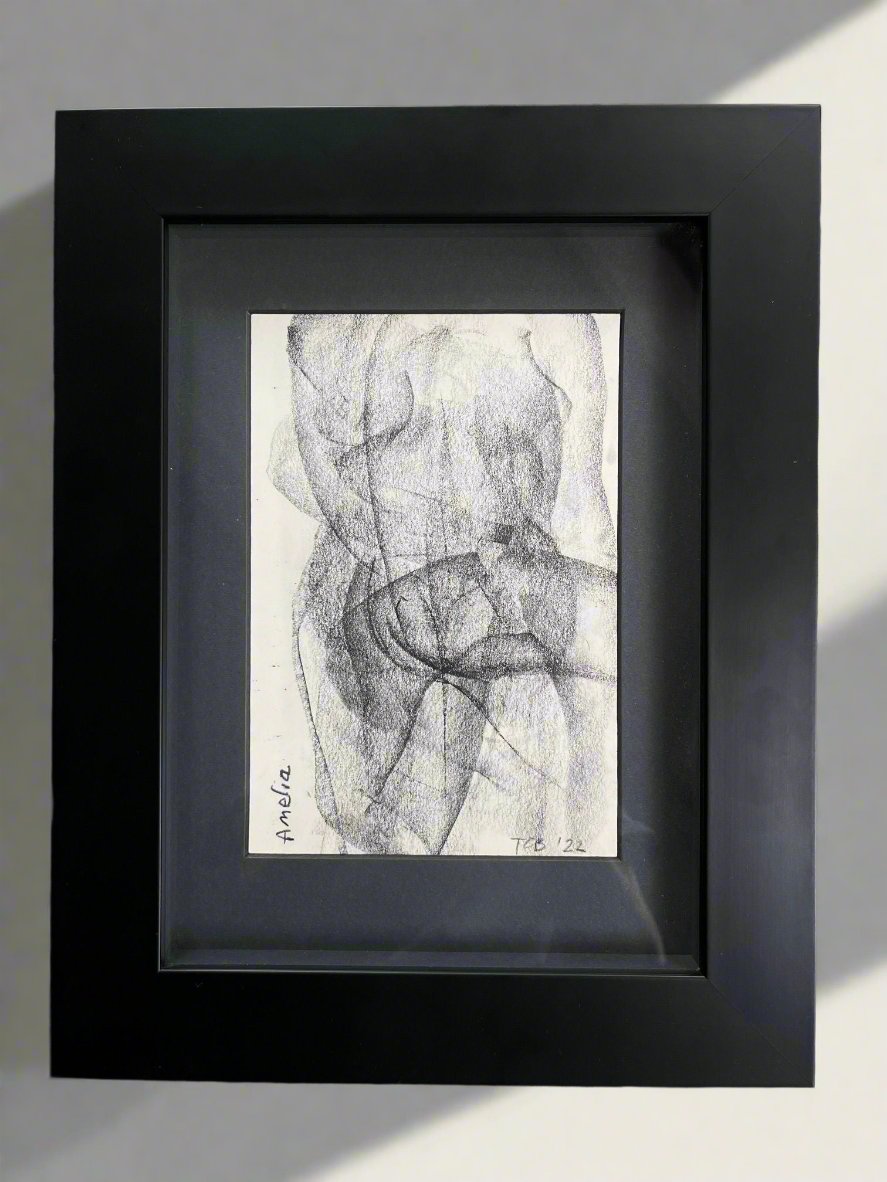 The product Croquis Drawing no.VII "Amelia" by Médecine showcases a contemporary English artist's framed charcoal drawing, characterized by overlapping, swirling lines that form a partial human figure. Displayed on a textured, dark leather surface, the artist’s signature and the year '22 are visible at the bottom left.