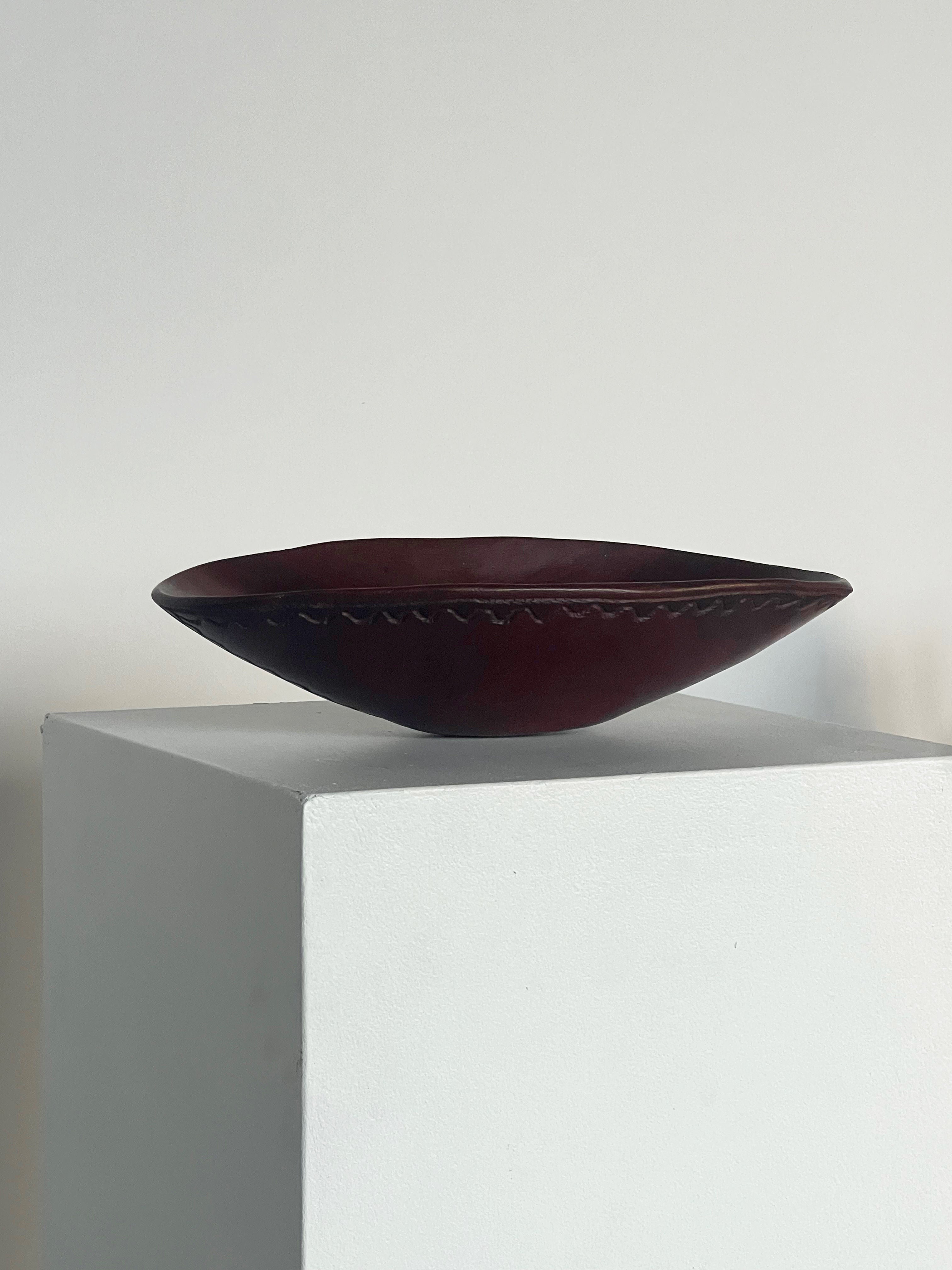 A Carved Wooden Bowl by Porter Studio, featuring shallow hand-carved designs along the rim, is displayed on a white pedestal against a simple light-colored background.