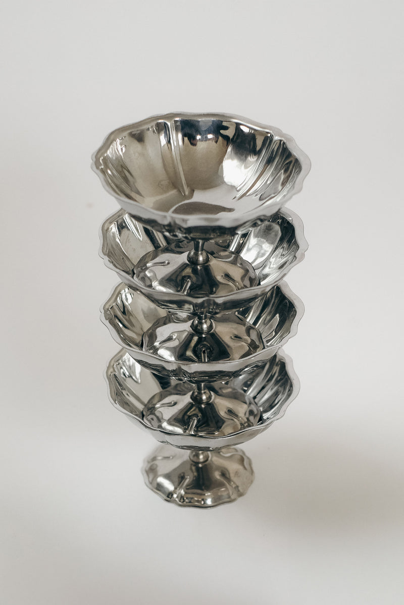 Stacked set of four polished silver ice coupes on white background