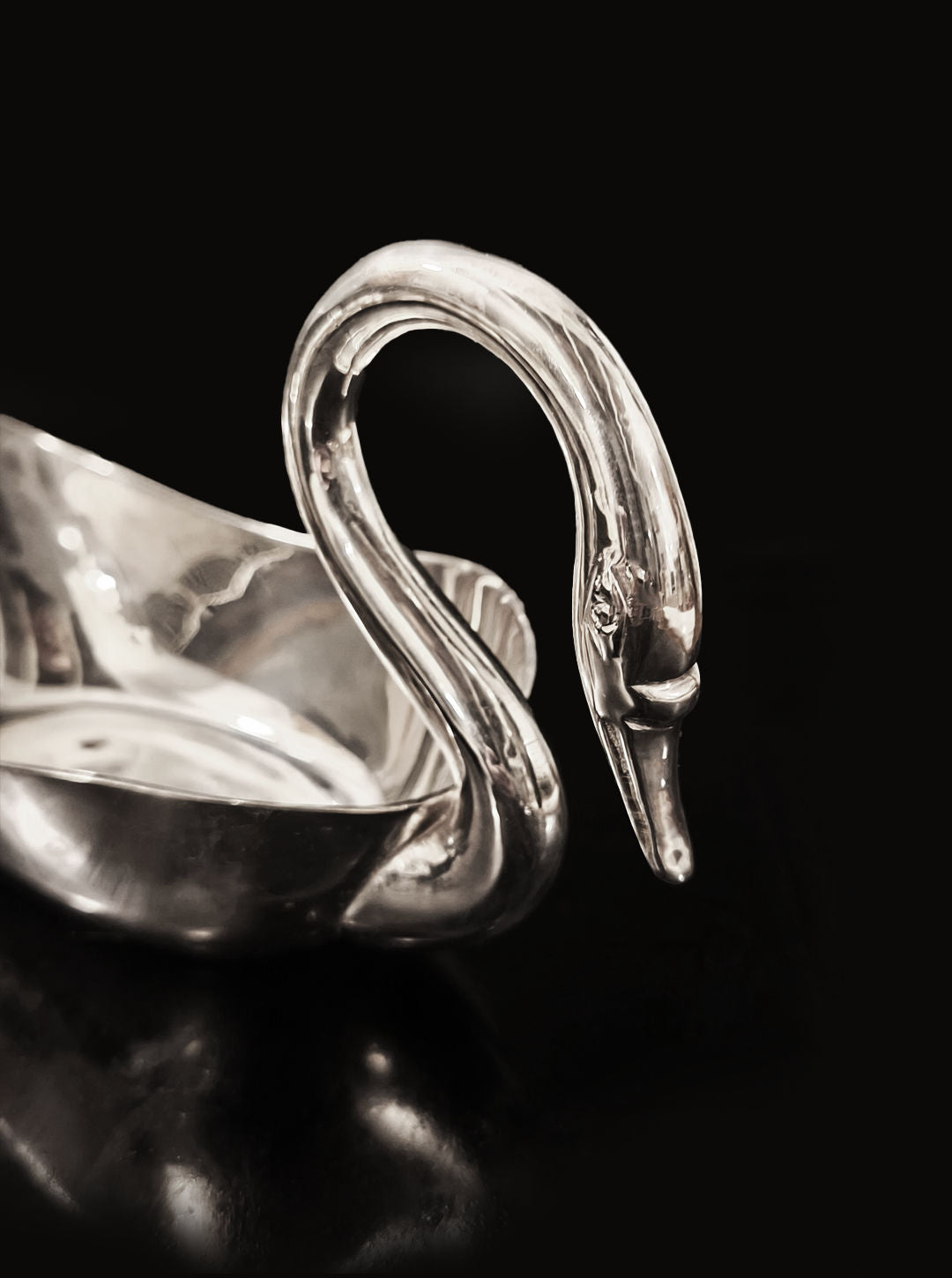 The Les Objoies Swan Silver Saucer, featuring a silver swan-shaped gravy boat with a long curved neck and intricate details, is beautifully presented on a matching silver-plated saucer against a dark backdrop.