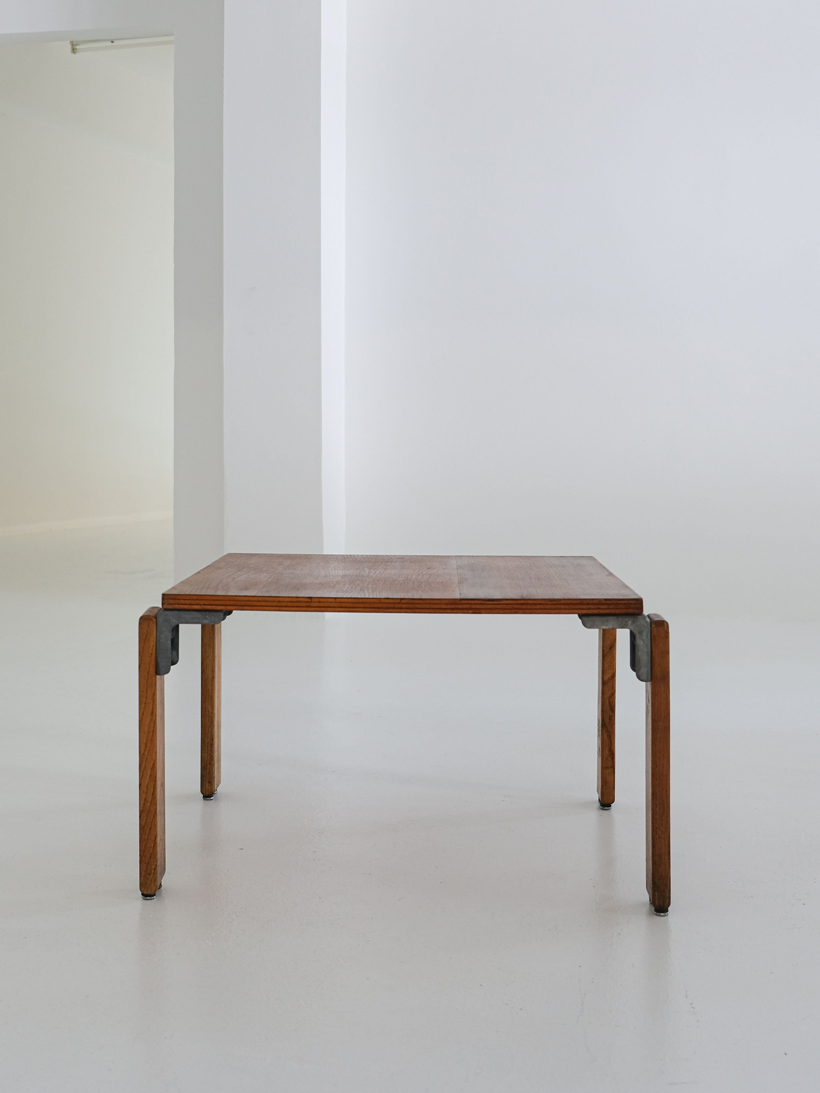 Standing against a white wall in a modern, brightly lit room is the Coffee Table by George Candilis and Anja Blomstedt, crafted in the 1970s for antibeige. Its minimalist design is complemented by metal brackets and an oak plywood finish atop a smooth, light floor echoing 1970s style.