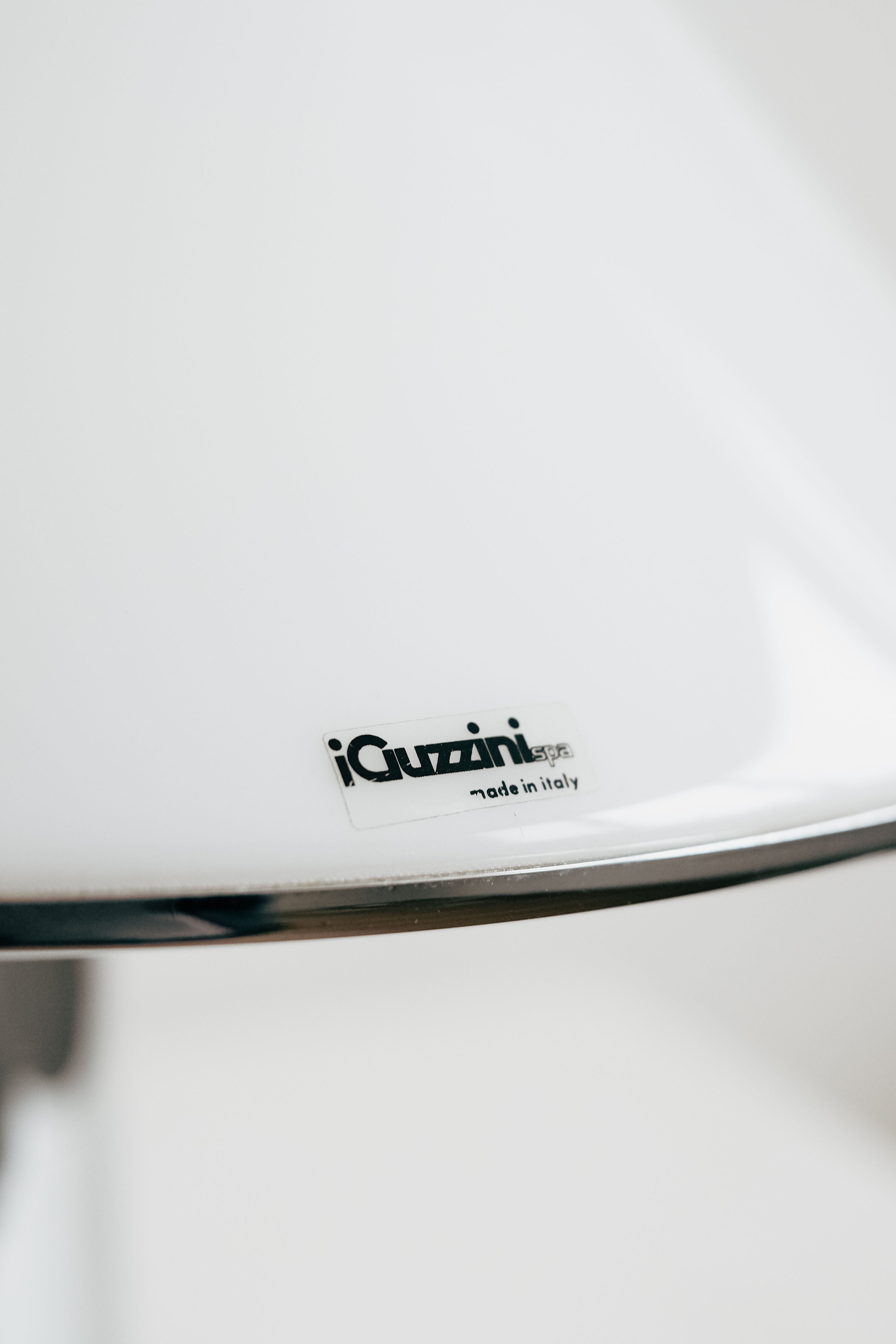 Close-up of a white surface with a metallic label, likely from a Harvey Guzzini Elpis Table Lamp by septembre studios. The blurred background emphasizes the brand and vintage style.