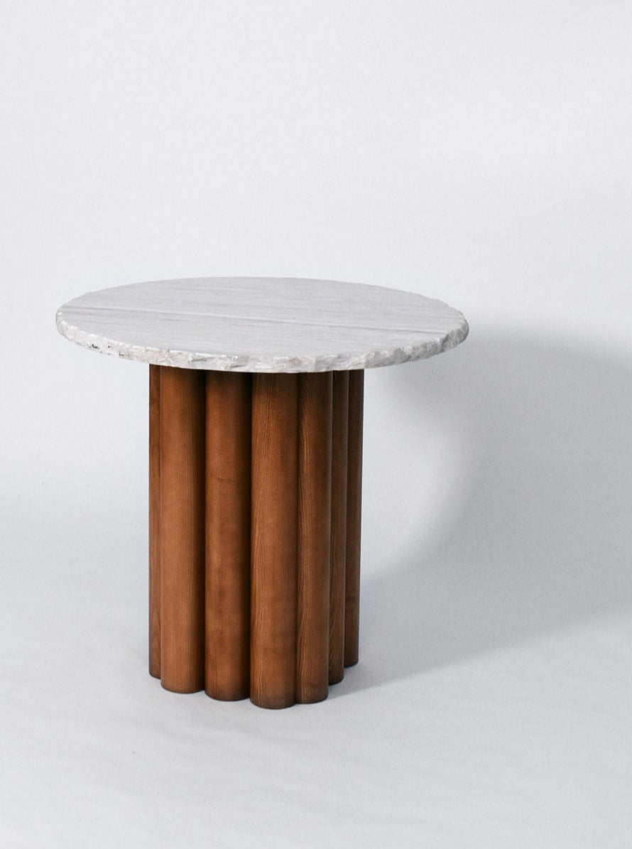 A round "Carrasqueira" table, Barracuda edition with a smooth, white marble top is supported by a base of vertically aligned cylindrical oak pillars. The background is a plain white surface, highlighting the table's minimalist, modern design from Barracuda Interiors.