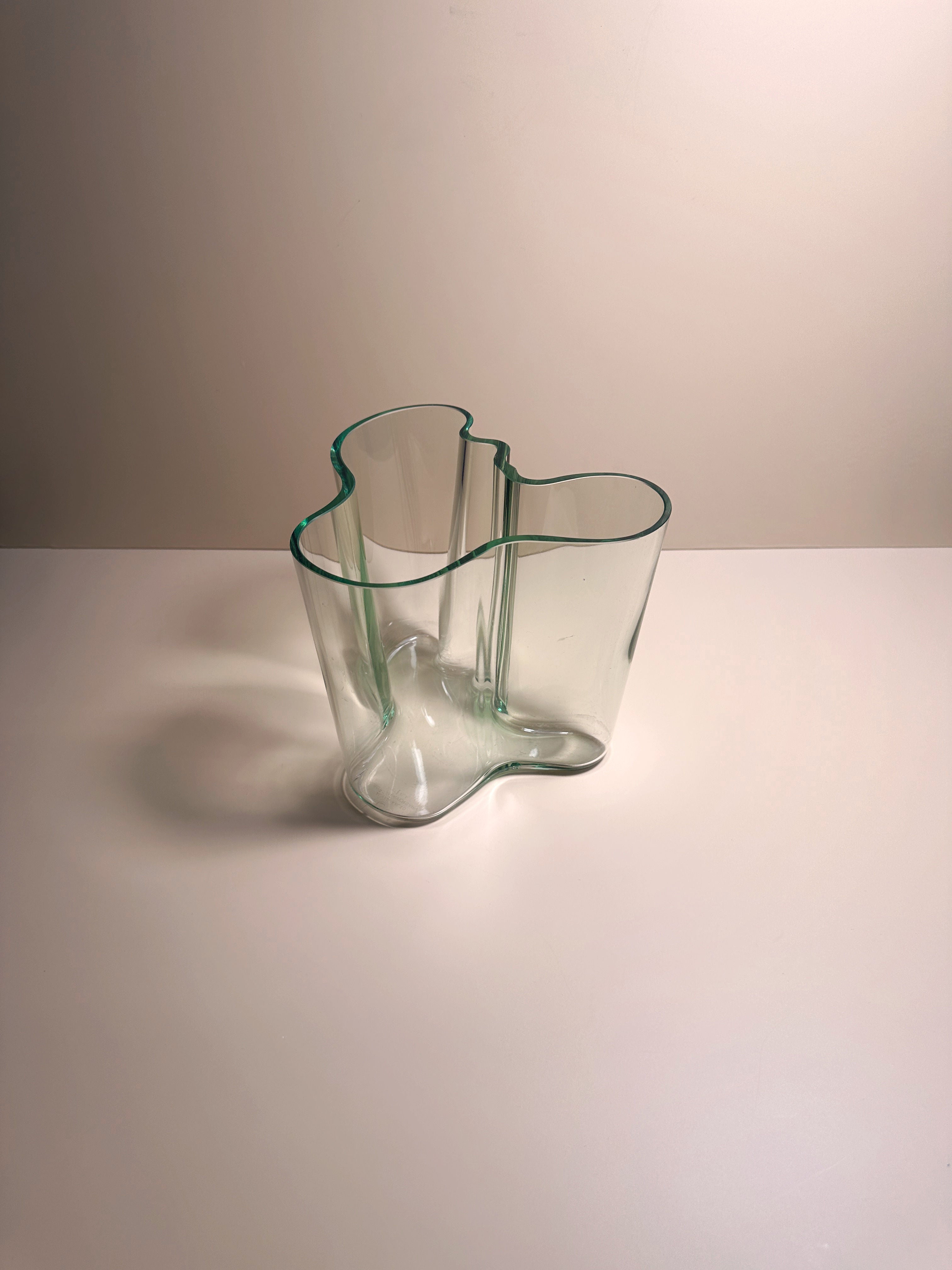 A translucent, curvy Limited Edition Aalto Vase from Dodo Vintage with an irregular, organic shape sits on a white surface against a light beige background. The vase's soft, flowing contours give it a modern and artistic appearance, making it a prized collector's item.