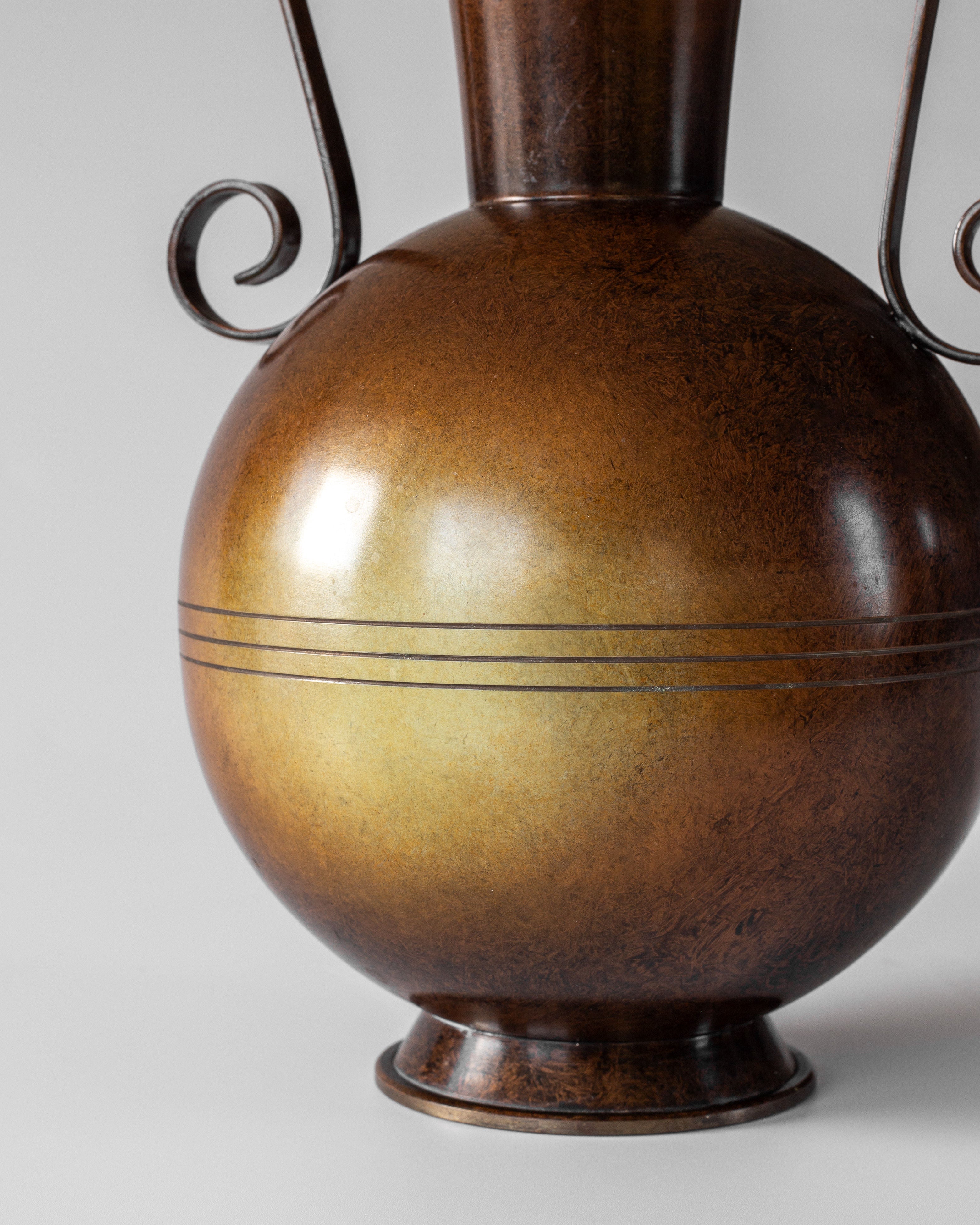 A close-up of a 1930s Spigel Swedish Art Deco bronze vase features a round, polished body with subtle gradient color, three decorative lines at its widest point, and two elegant, curved handles on either side.