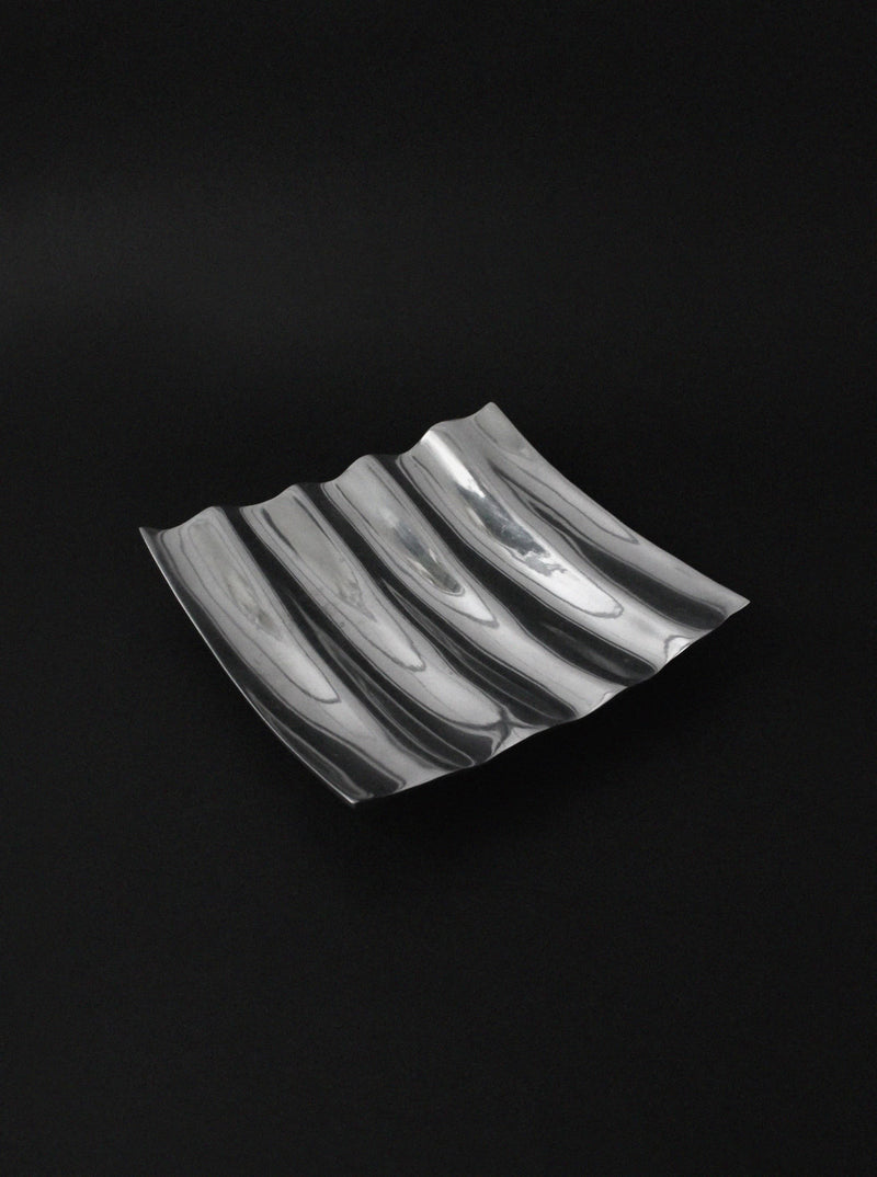 Polished aluminum wave bowl with curved ridges on black background