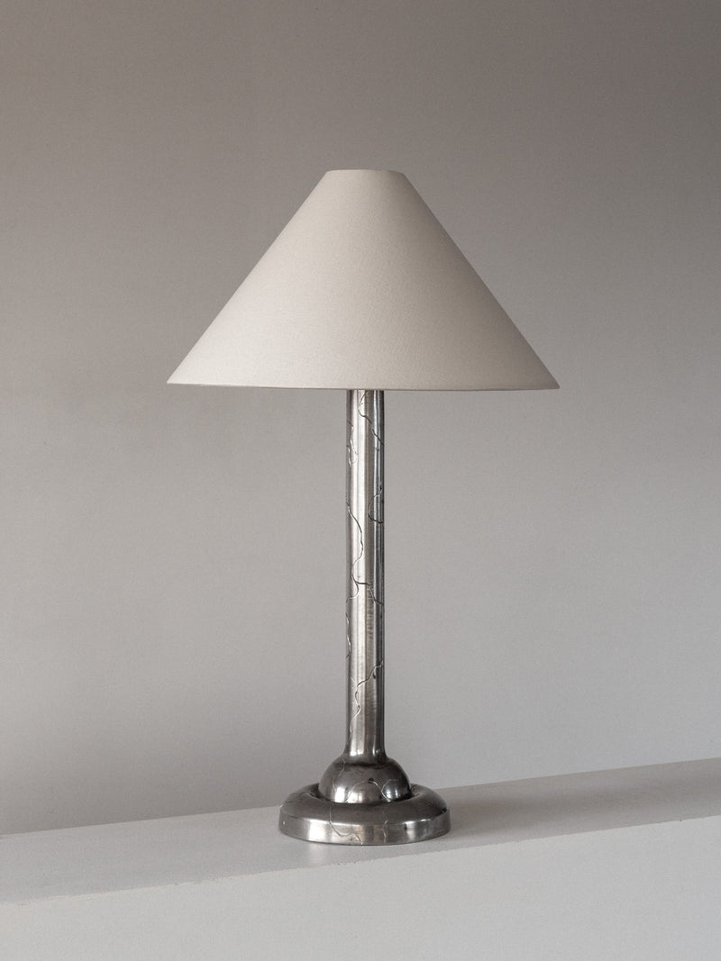 The Spigel Art Deco Pewter Lamp from 1920s Sweden features a cone-shaped white shade and metallic base, set on a white surface against a plain gray background.
