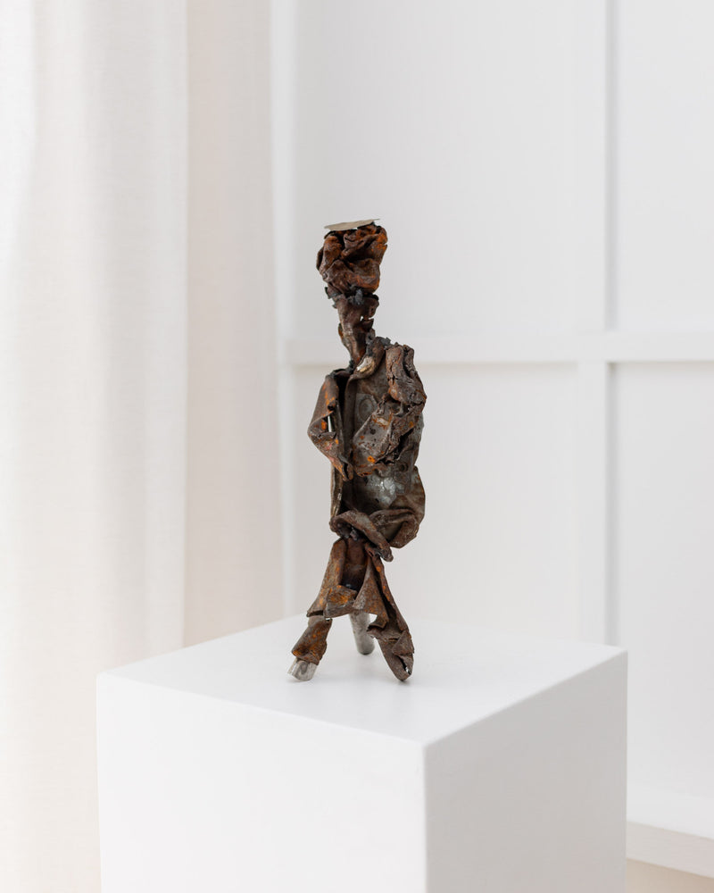 The Metal Sculpture - Italy 1970s by Bottega Jacobs is a small, brutalist piece with a twisted, textured look. This handmade sculpture is showcased on a vintage white pedestal against a light-colored background.