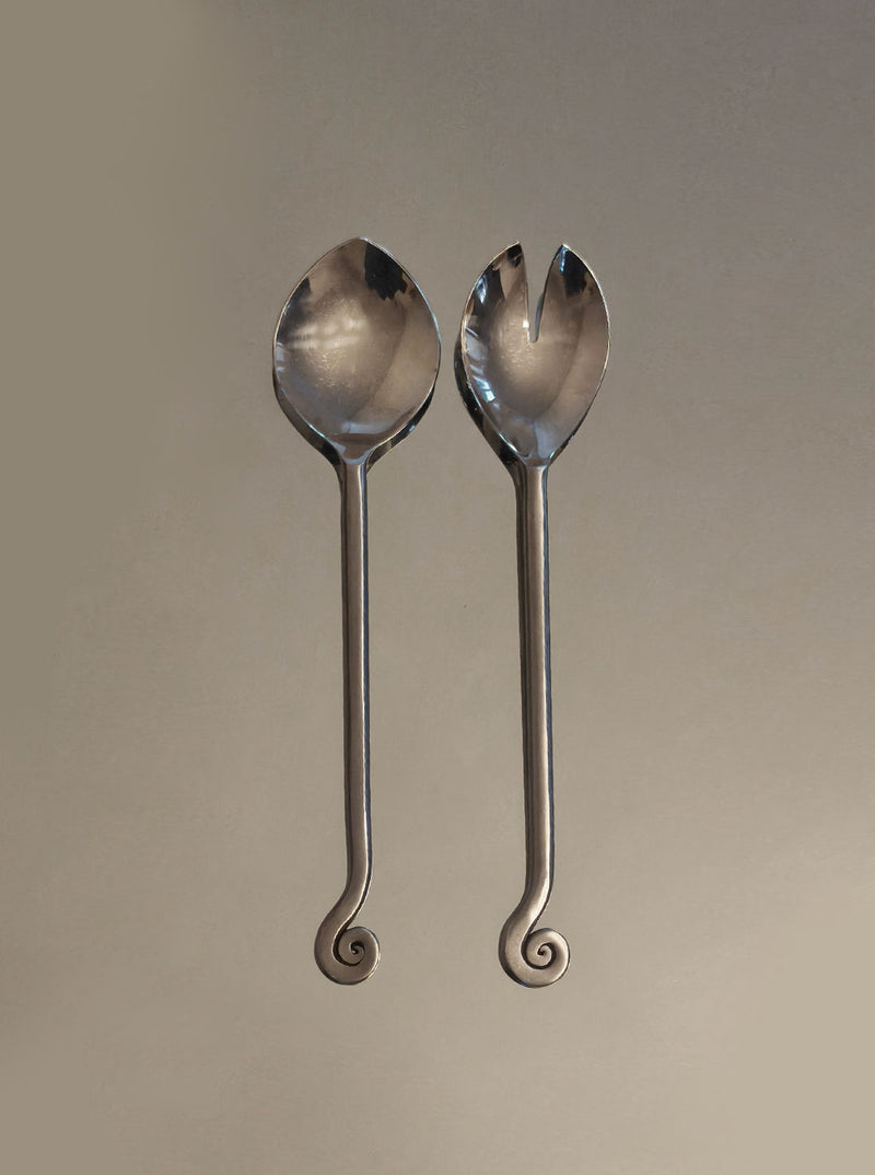 The Les Objoies Spiral Salad Servers feature long handles with spiral ends—one solid spoon, one forked—for a sculptural, decorative touch that stands out against a neutral background.