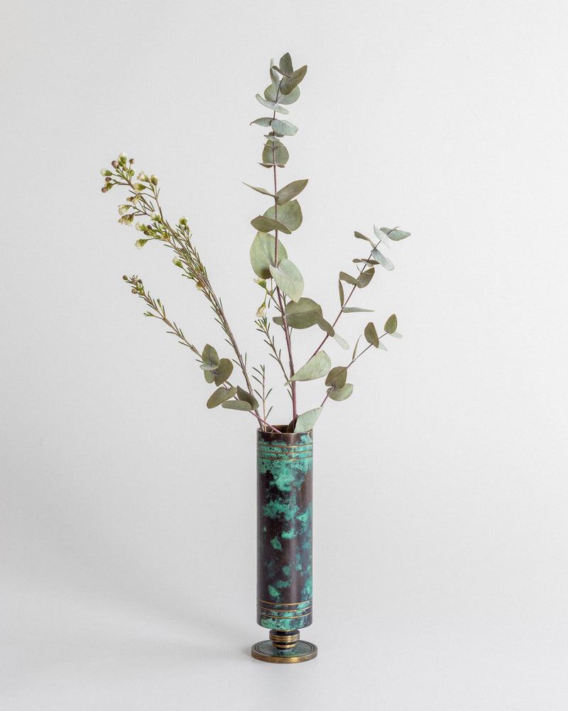 A minimalist arrangement of eucalyptus and small white flowers in Spigel’s Art Deco Bronze and Brass Vase, inspired by 1930s design, set against a plain white background.