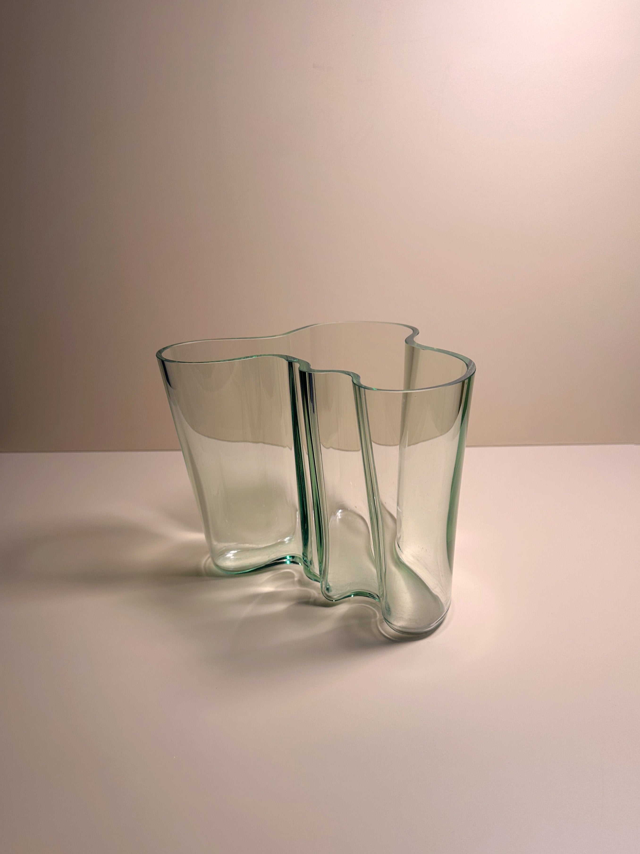 A modern, abstract Limited Edition Aalto Vase from Dodo Vintage with a wavy, sculptural design is shown against a plain background. This piece features a clear and slightly greenish tint, giving it a sleek, contemporary appearance. The vase's undulating form creates an organic, fluid look, making it a coveted collector's item.