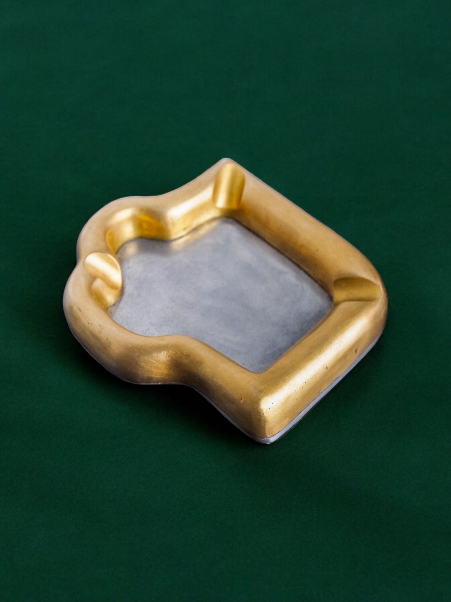 This intriguing Brutalist "Puzzle" Ashtray, designed by David Marshall and crafted in Spain in 1970 for Malamar Studio, features a bronze and aluminum composition shaped like a bitten slice of toast, elegantly positioned on a dark green surface.