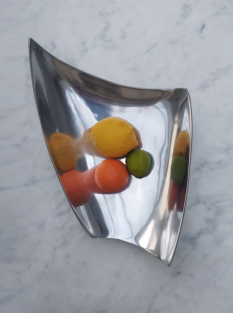 A modern, asymmetrical Les Objoies Brass 80's Large Tray containing various citrus fruits, including lemons and limes, displayed on a marble surface.