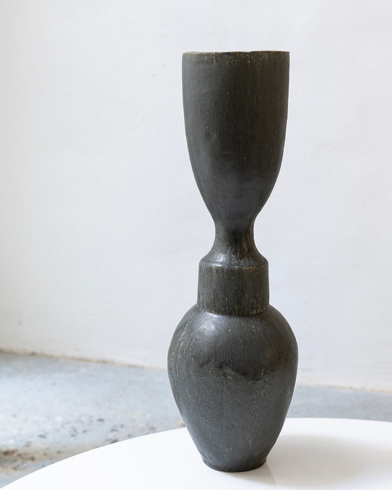 The 'Isolated n.36' Vase by Canoa Lab is a tall, dark matte ceramic vessel with a narrow middle and rounded base, handcrafted and shown on a white surface against a plain light gray background.