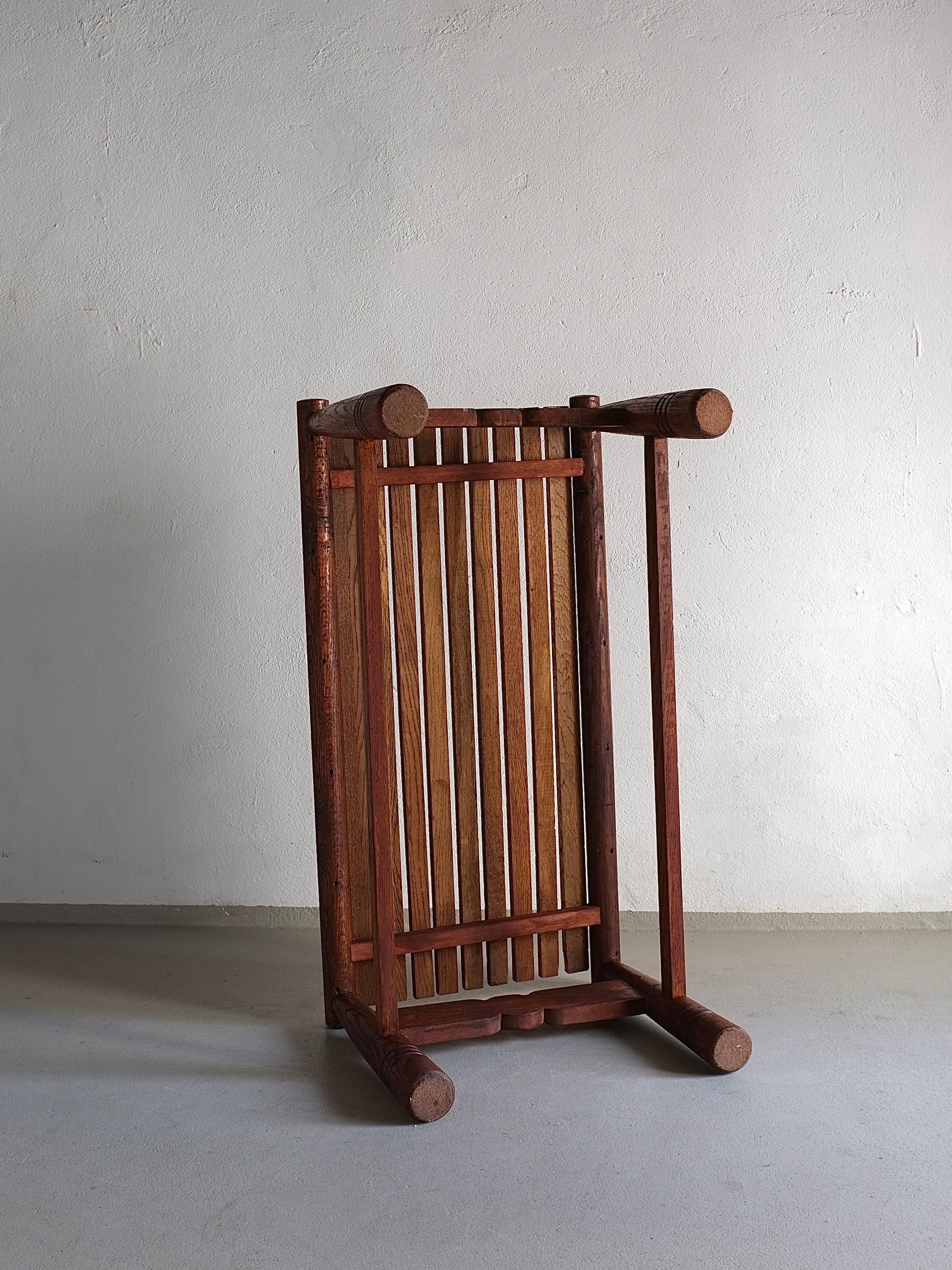 A vintage-condition Carved Dark Oak Bench from the 1960s by Veter Vintage is positioned upside down against a plain white wall. The bench features a slatted seat and cylindrical legs, showcasing its natural wood texture. The minimalist setting highlights the design and craftsmanship of this timeless piece from France.