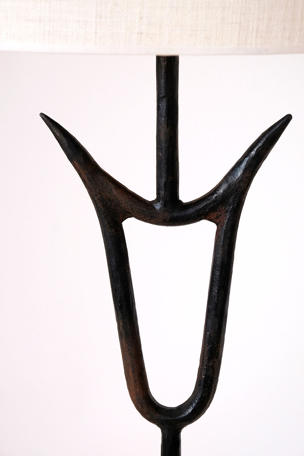 Close-up of the "Sevilla" Lamp by Barracuda Interiors, an artistic bull lamp base made of dark, zoomorphic hammered iron with an abstract design. The base features two upward-facing, curved prongs connected by a central vertical rod, creating a unique, symmetrical shape against a plain white background.