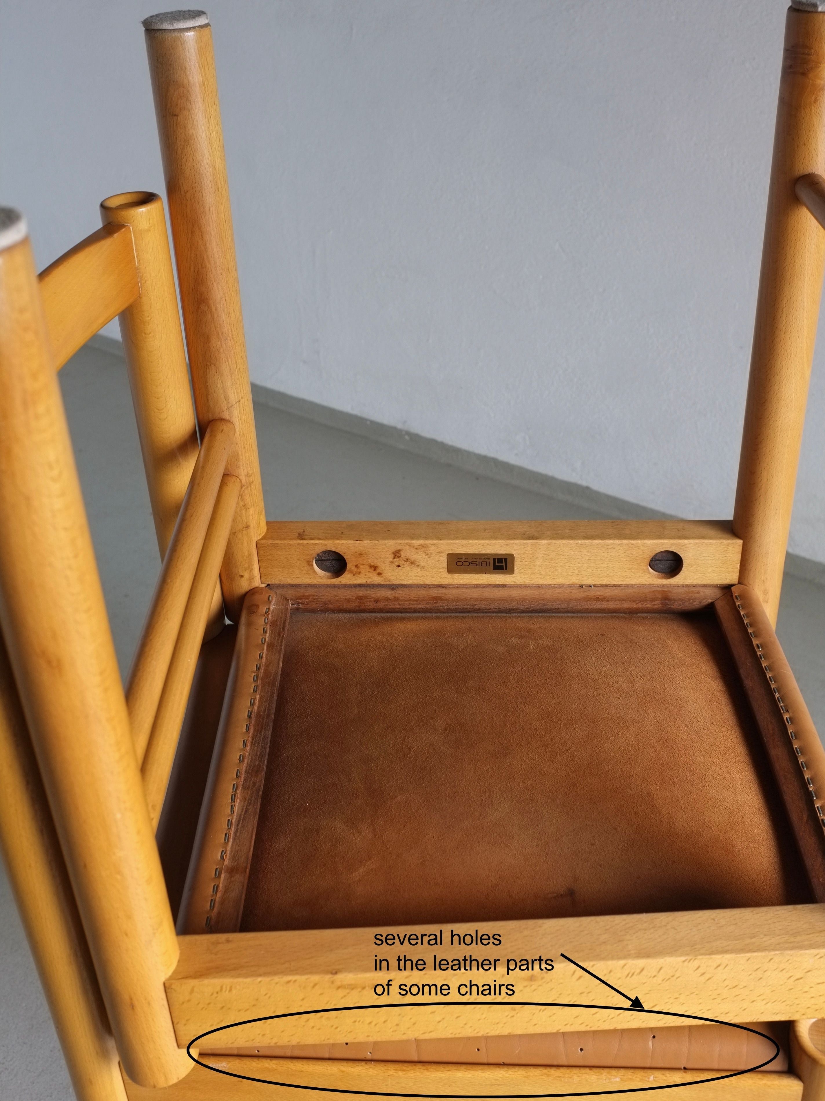 A set of 6 beech wood chairs from Veter Vintage, featuring cognac leather seats, originating from Ibisco, Italy in the 1960s. The chairs display their vintage condition with several small holes in the leather sections, clearly marked by a black oval and annotated with "several holes in the leather parts of some chairs.