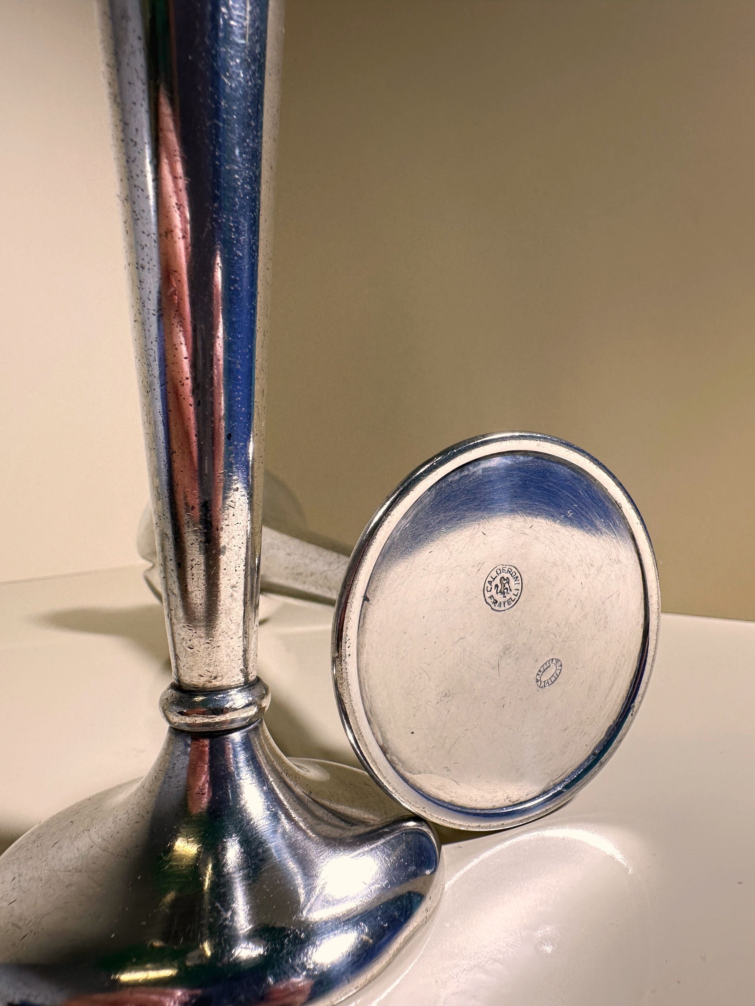 A close-up of an Alpacca silver trophy with embossed details emerges on a white surface. The neutral backdrop accentuates its reflective quality, akin to the 1930s Set of 2 Candlesticks by Gio Ponti for Calderoni from Dodo Vintage.