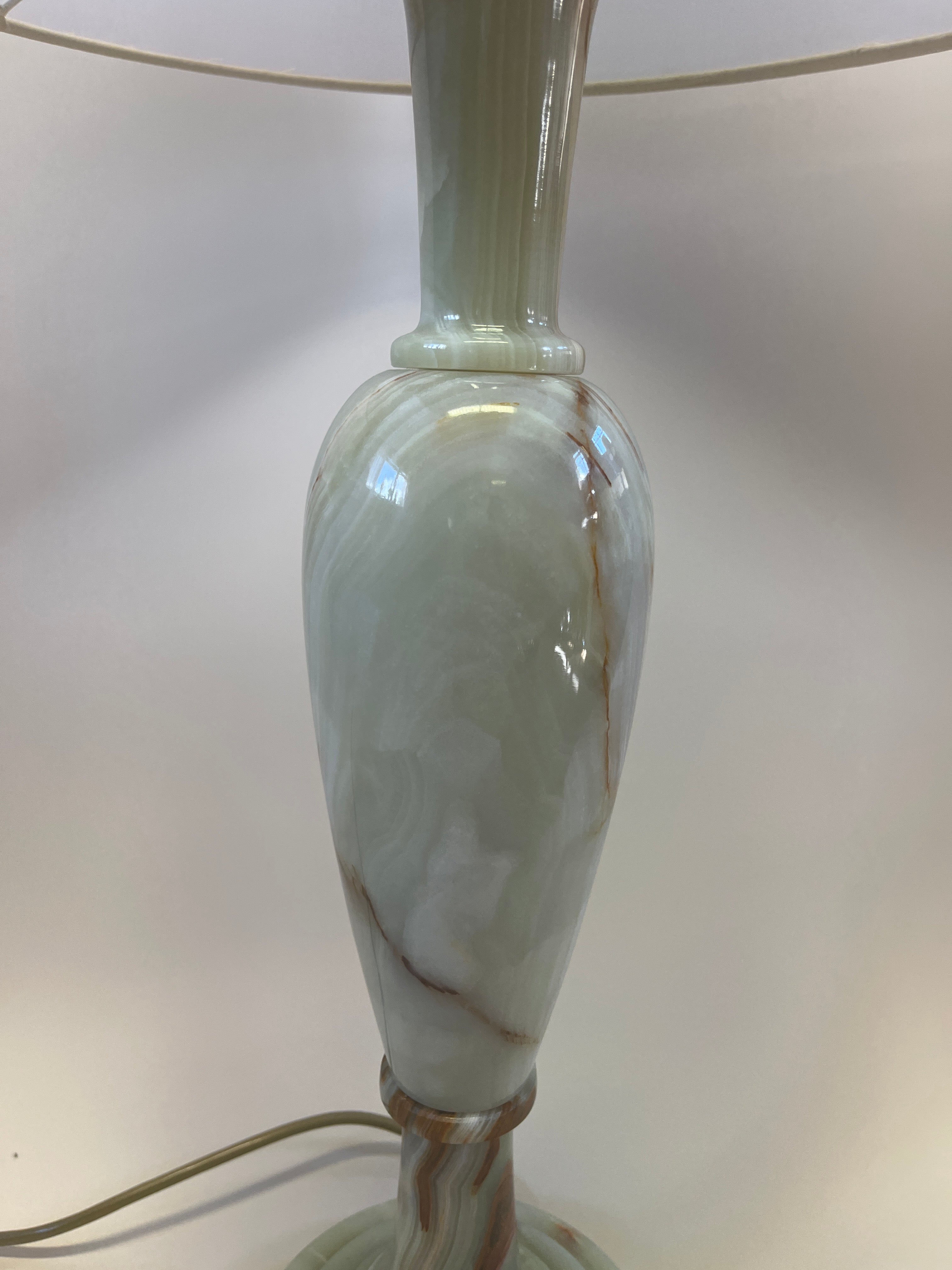 A close-up of the Maud Vaughan Large Vintage Onyx Lamp showcases its elegant design with a marble-like base in white and light brown hues. This exquisite lamp features a smooth, rounded shape with a subtle sheen that accentuates the marbled pattern. The antique gold flex cord is visible at the bottom, adding a touch of vintage charm.