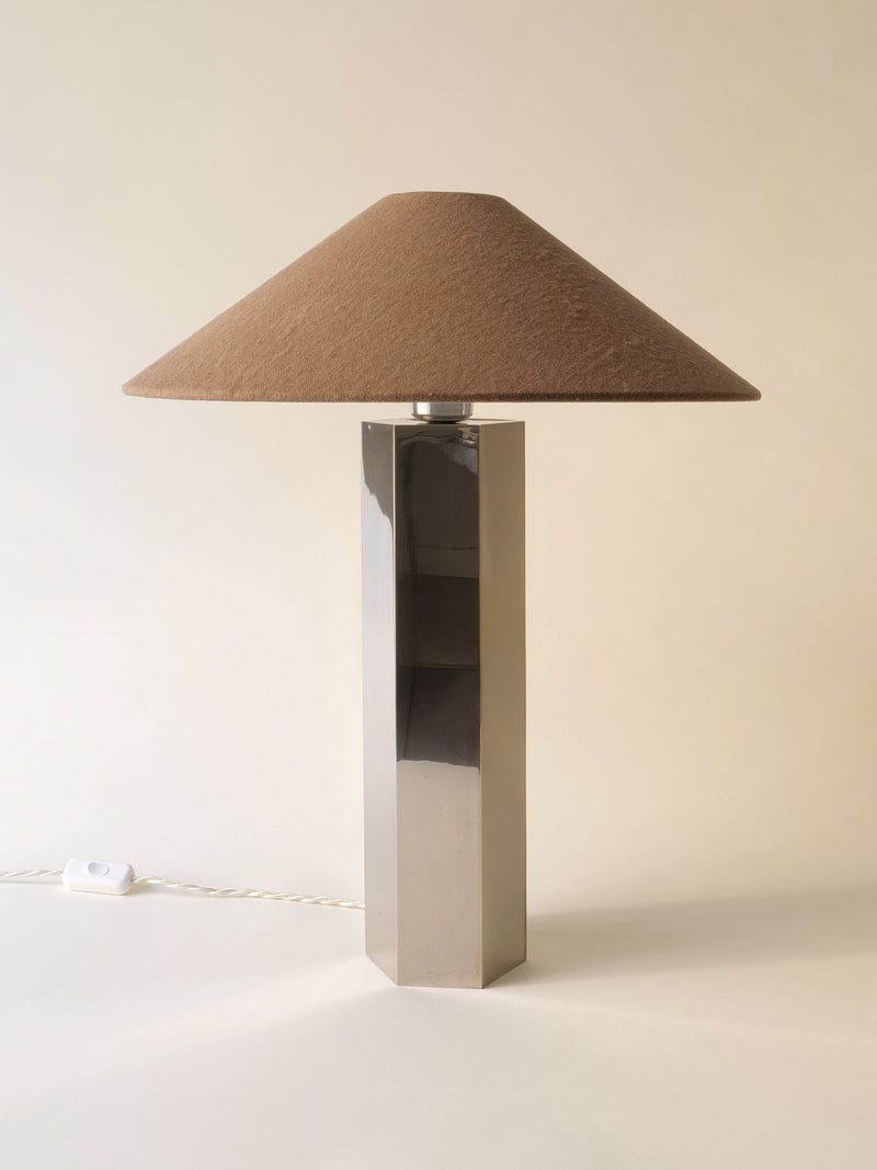 The Grand Hexagonal Lamp by Collection apart features a tall metallic base and wide brown conical shade. A white cord with switch lies on the light surface, set against a plain background that highlights this stylish 1970s design.