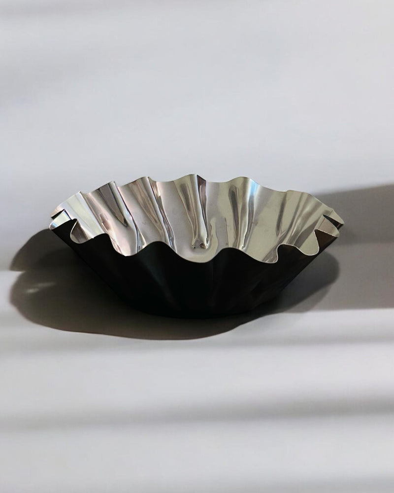 Wavy metallic bowl casting dramatic shadow on white surface